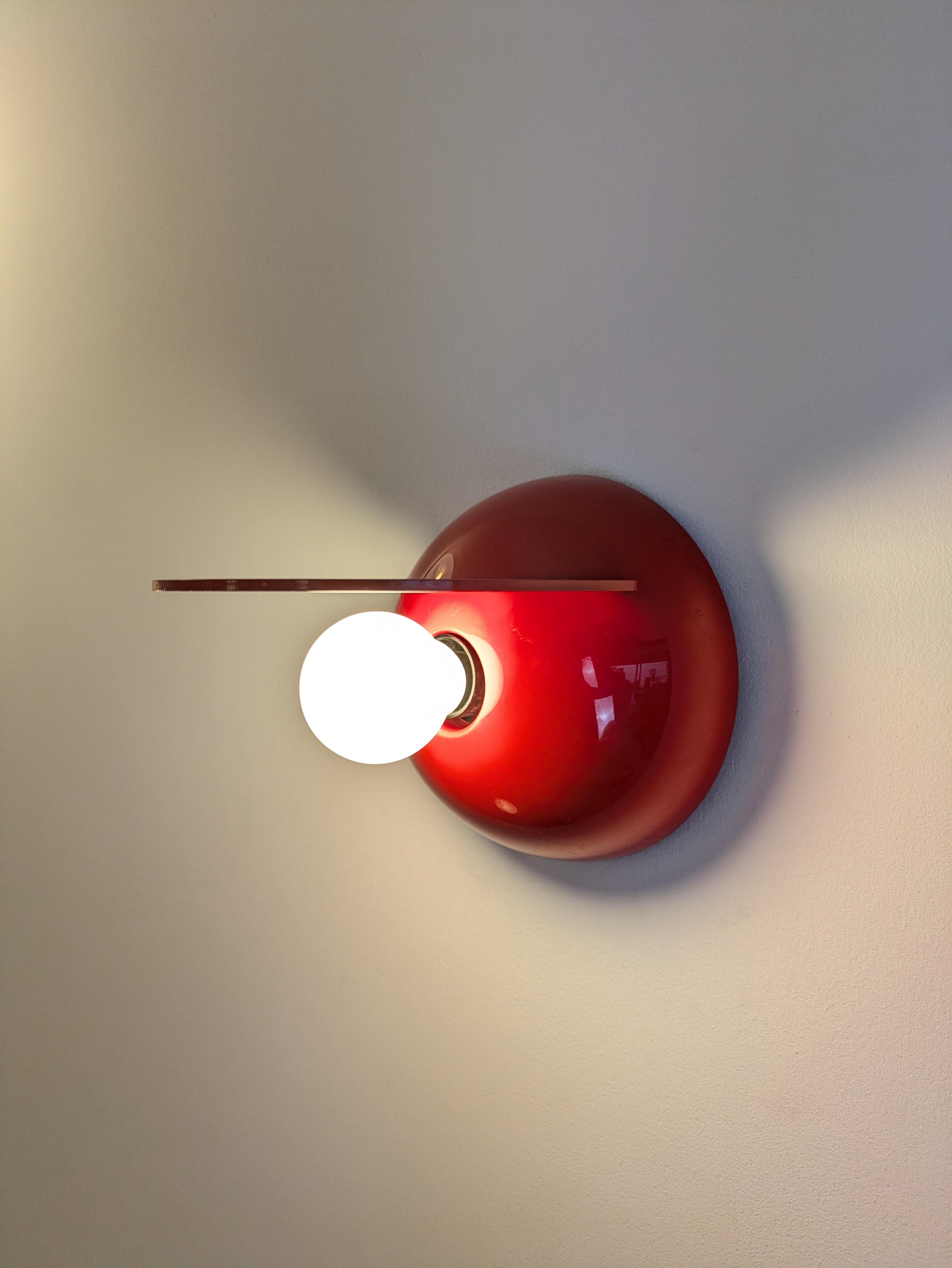 Este aplique Buco (Agujero) es de fabricación italiana y está fabricado por Artemide. Fue diseñada por el diseñador italiano Claudio Dini. 
Está hecha de plástico rojo ♥️ (ABS) sobre un soporte de plástico negro que permite que la parte roja
