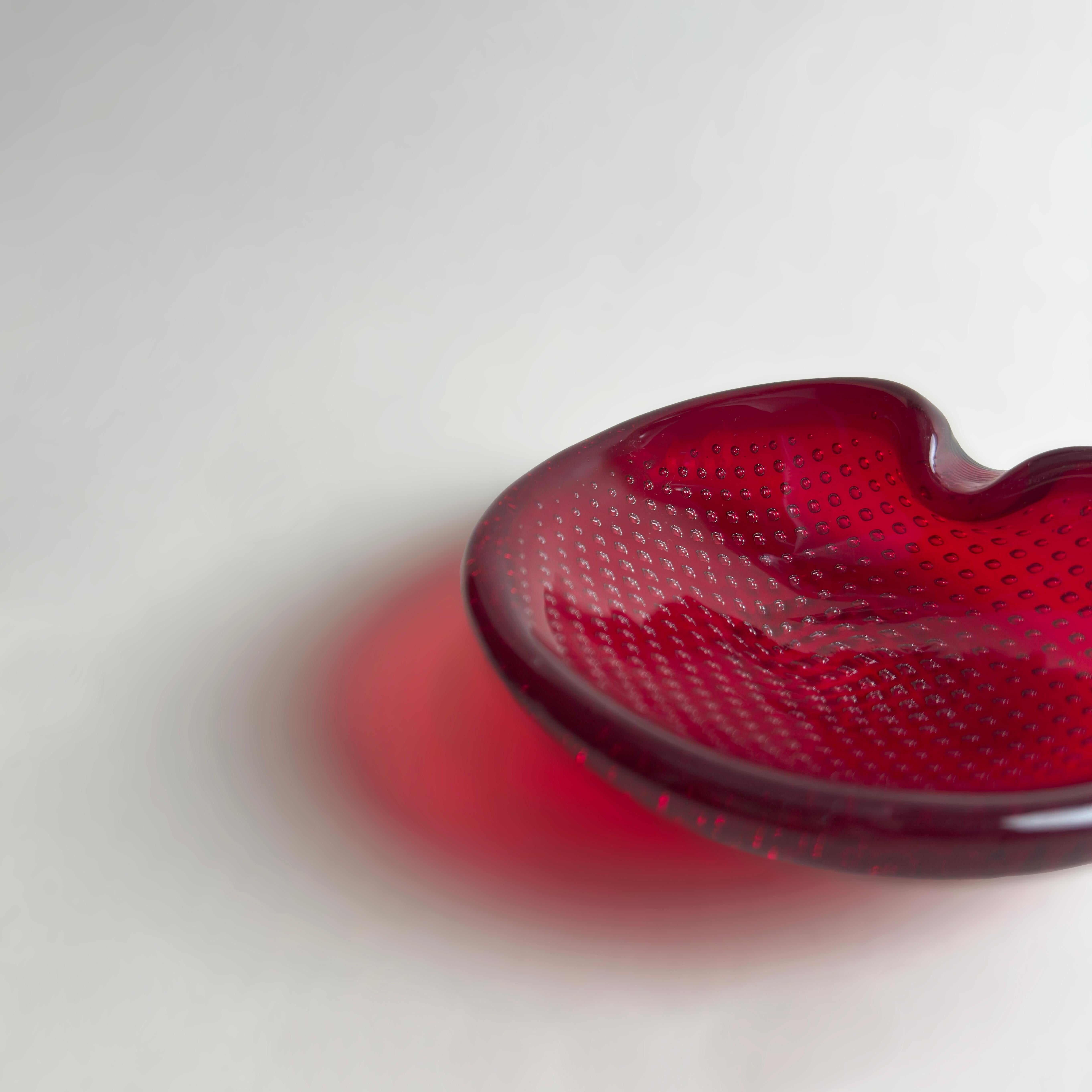 A hand-blown Murano glass ashtray crafted in the 1960s by Venetian maestro Archimede Seguso. Oval in form, the compact dish is made from vivid red glass and features the bullicante technique—rows of evenly spaced bubbles suspended within the glass,