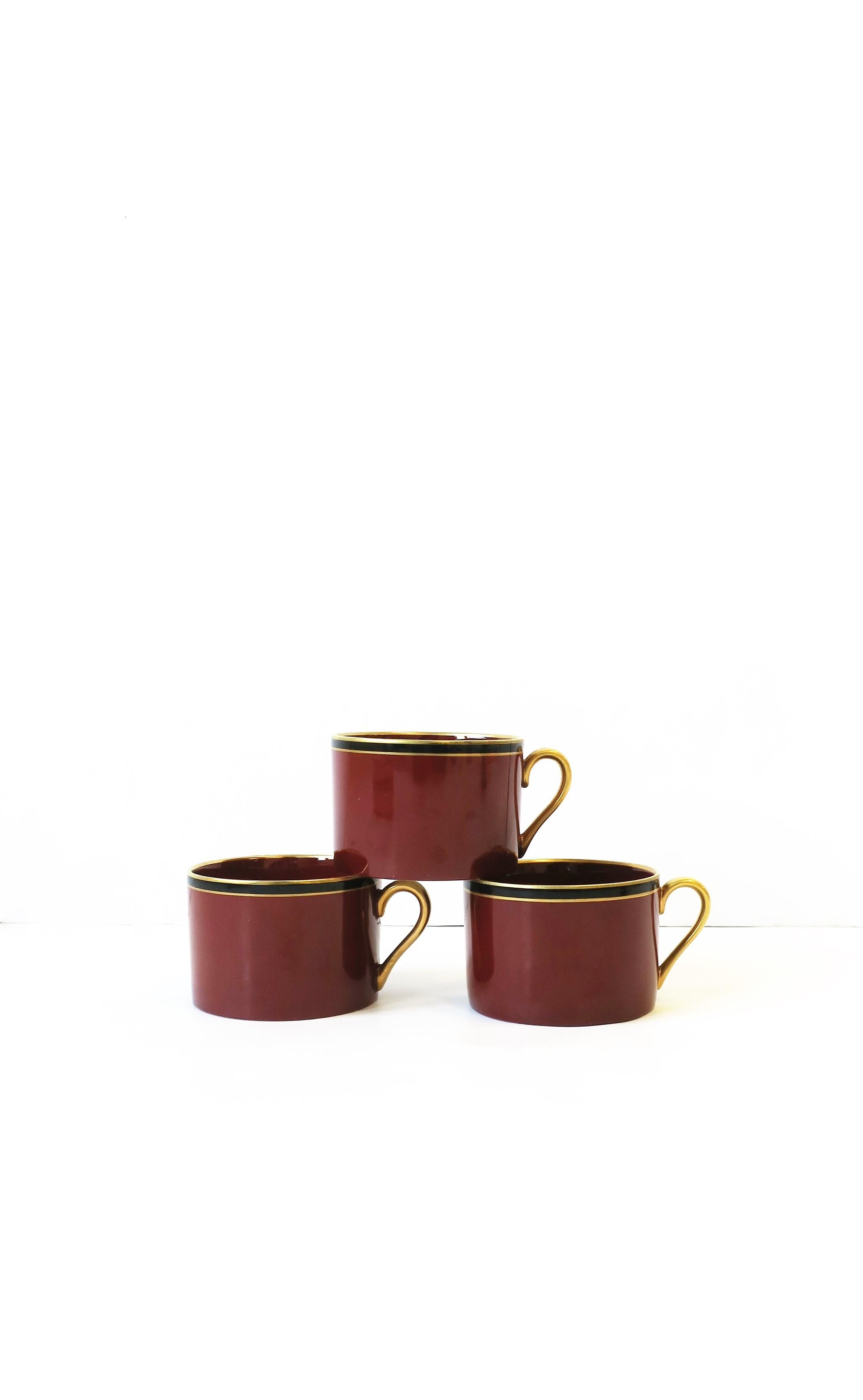 A chic set of three (3) vintage red burgundy, gold, and black porcelain coffee or tea cups, Mid-20th century, 1967. 

Side tables shown in image search 1stDibs ref. #s: LU1314221845702, LU1314221786072 (SOLD.)
Black Italian leather chair(s) shown,