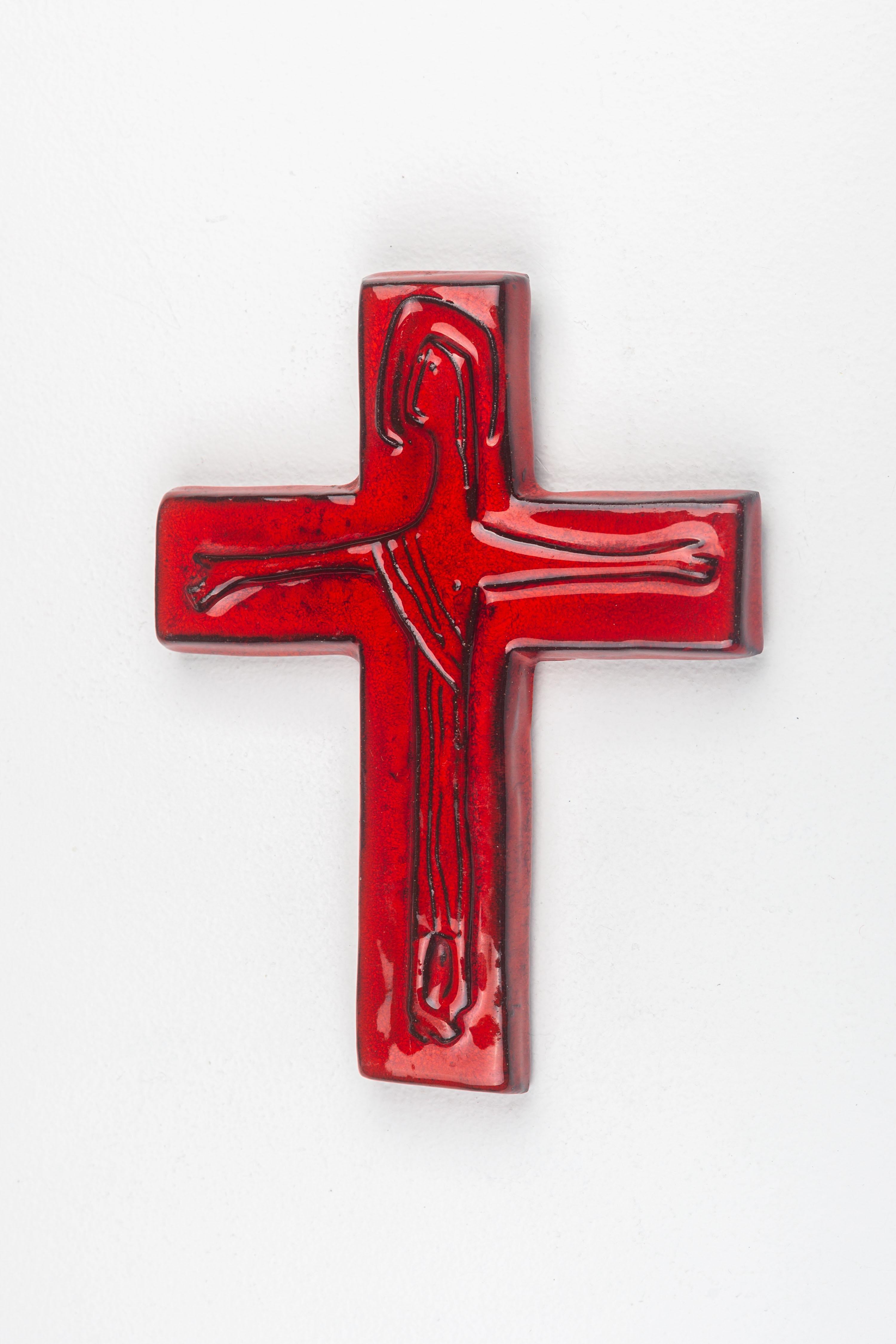 This mid-century modern ceramic crucifix, handcrafted by a European studio pottery artist, embodies the era's distinctive combination of traditional symbolism and modernist design. The piece features a vivid, glossy red glaze that covers the