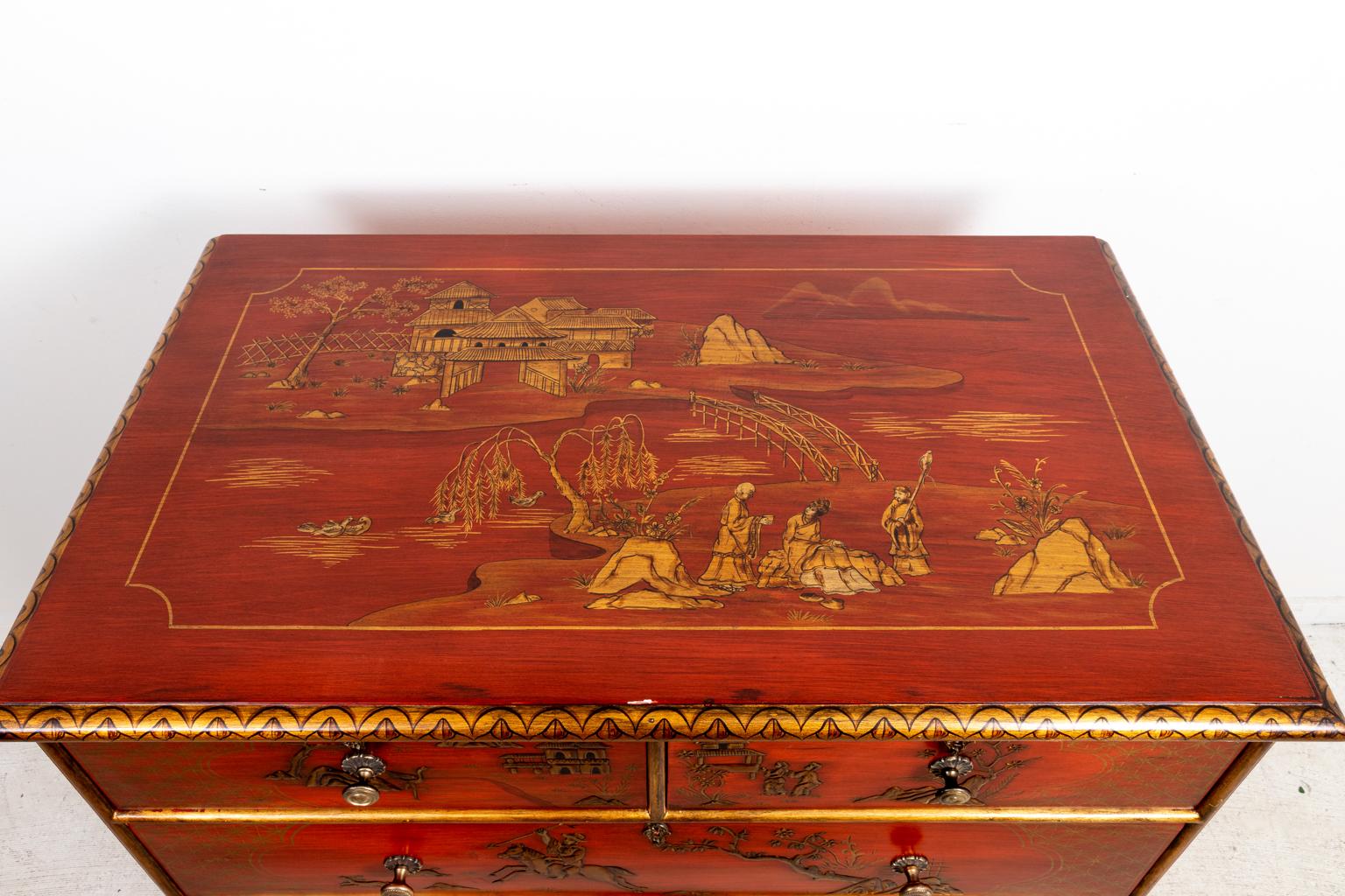 Red painted Chinoiserie style chest of drawers on bun turned feet with gold painted foliage trim throughout. The piece is constructed with two small over three large drawers. The drawer fronts are painted with motifs of Chinoiserie style figures on