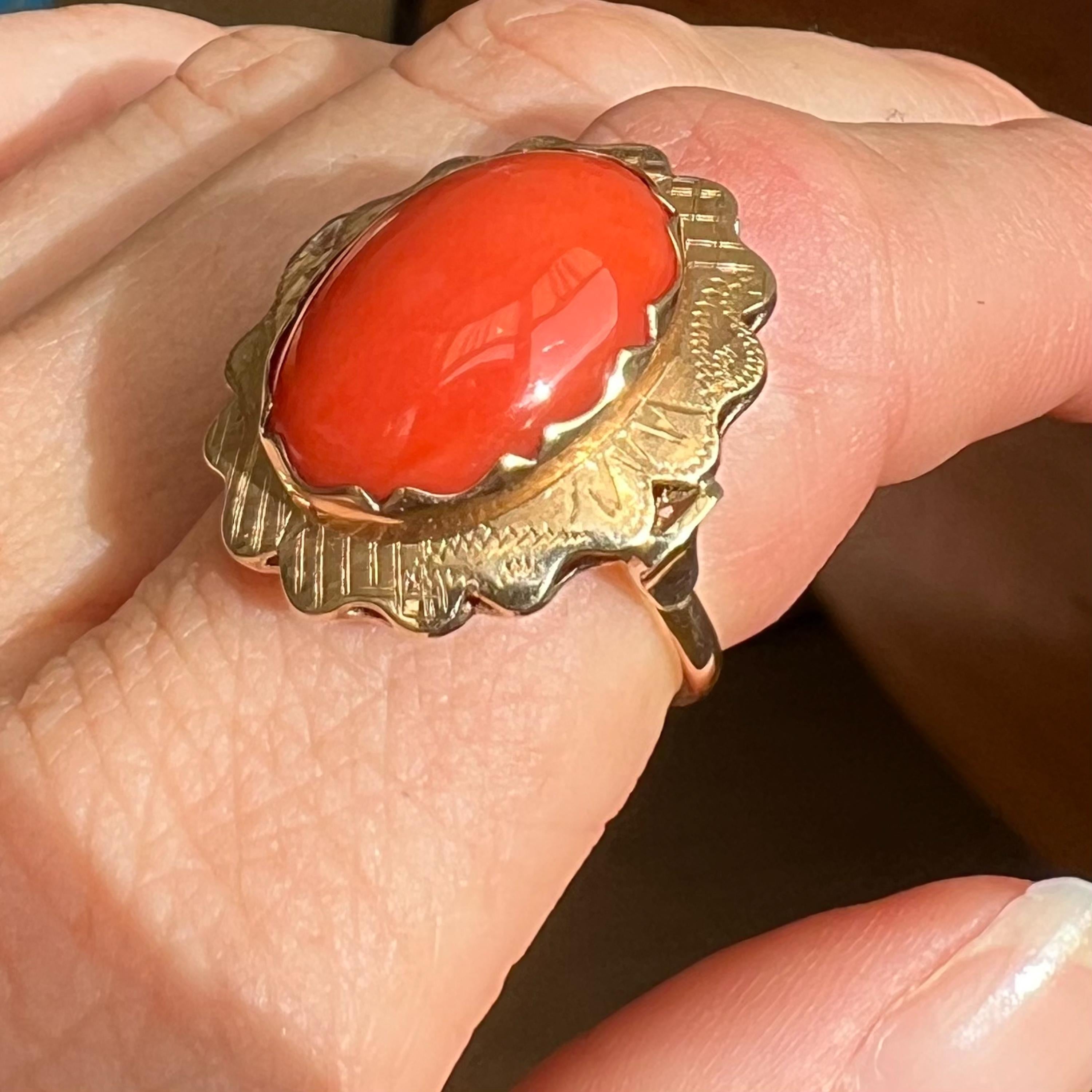A natural red coral ring set in a 14 karat gold oval-shaped mounting. The coral is bezel set in this 14 karat gold worked and engraved mounting. The prongs have a scalloped design and fit beautifully around the oval-shaped stone. The ring is