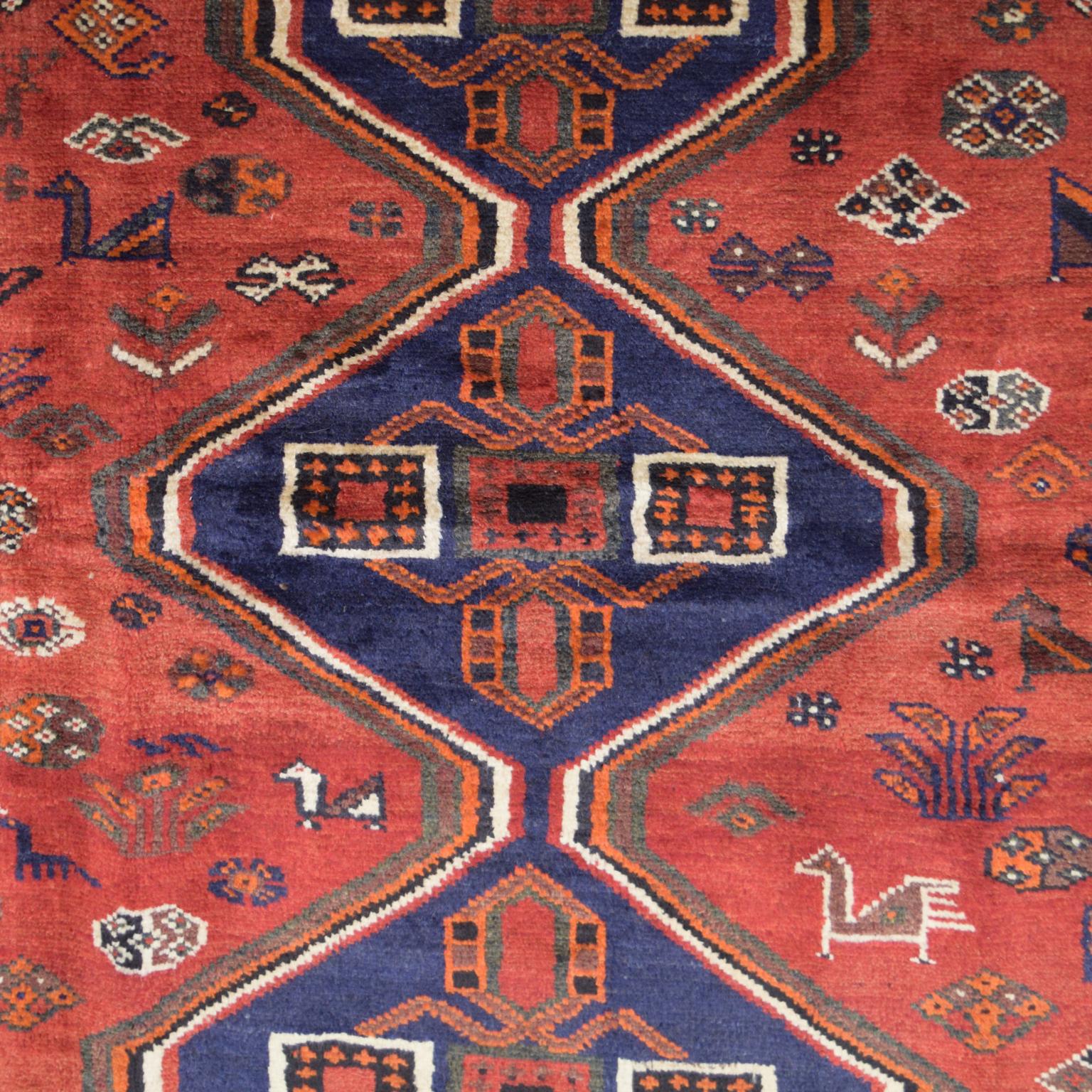 Measuring 5’3” x 7’1”, this Persian Ghashghai carpet in shades of red, blue, green, cream, and orange wool, is hand-knotted and belongs to Orley Shabahang’s World Market Collection. To craft this carpet, the weaver utilized a Persian weaving