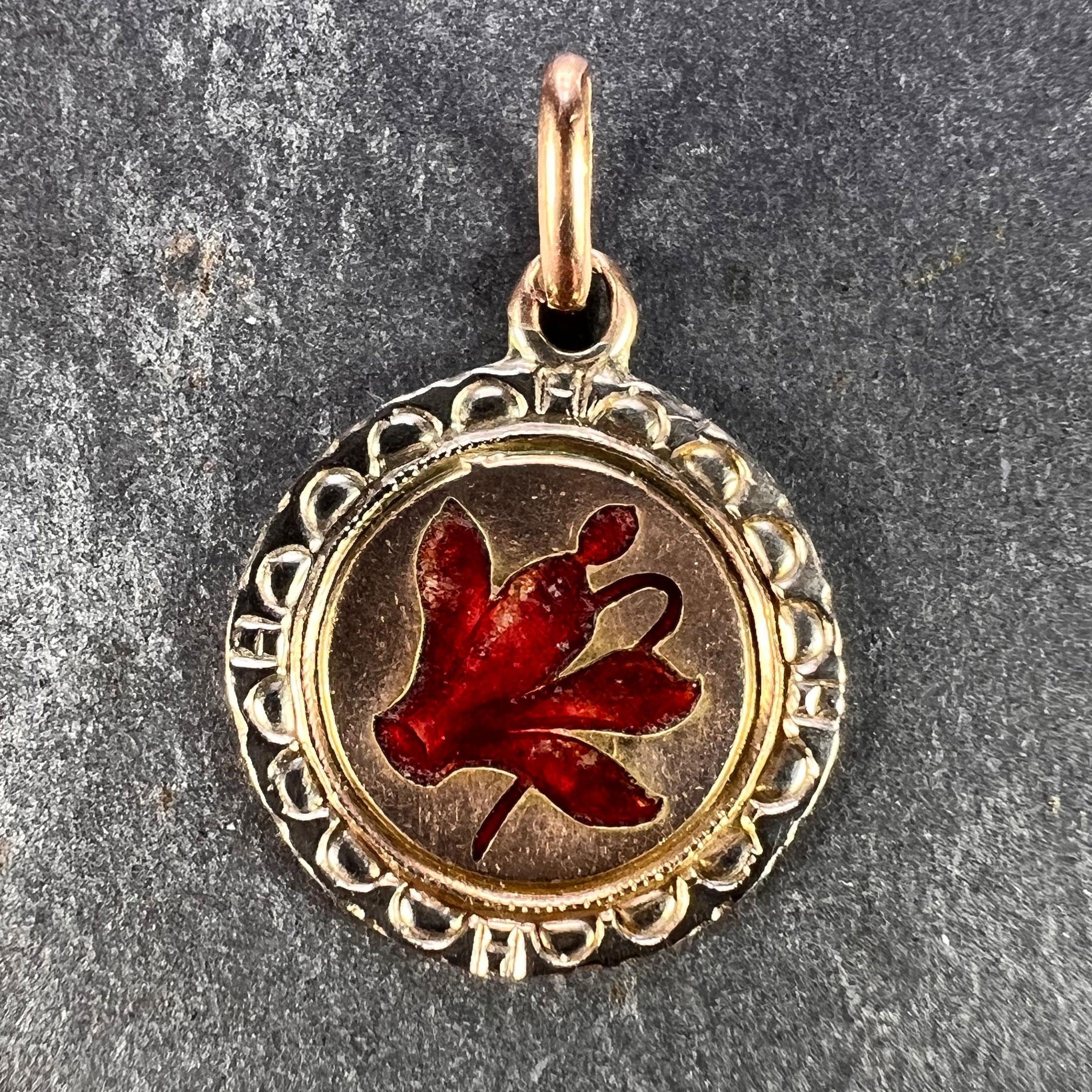 A 12 karat (12K) yellow gold charm pendant designed as a disc depicting a red enamel cyclamen surrounded by an intricate engraved white gold border. The cyclamen flower represents love and tenderness. Stamped with a French import mark to the pendant