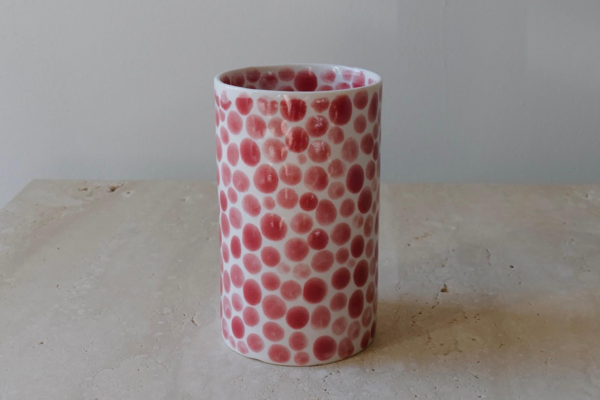 Ceramic drinking cup. Hand-cast in porcelain and once bisque fired, each dot is hand-painted with a shiny red glaze. An unconventional layered glazing technique, developed by the artist, is used in these cast porcelain pieces. The straight walls and