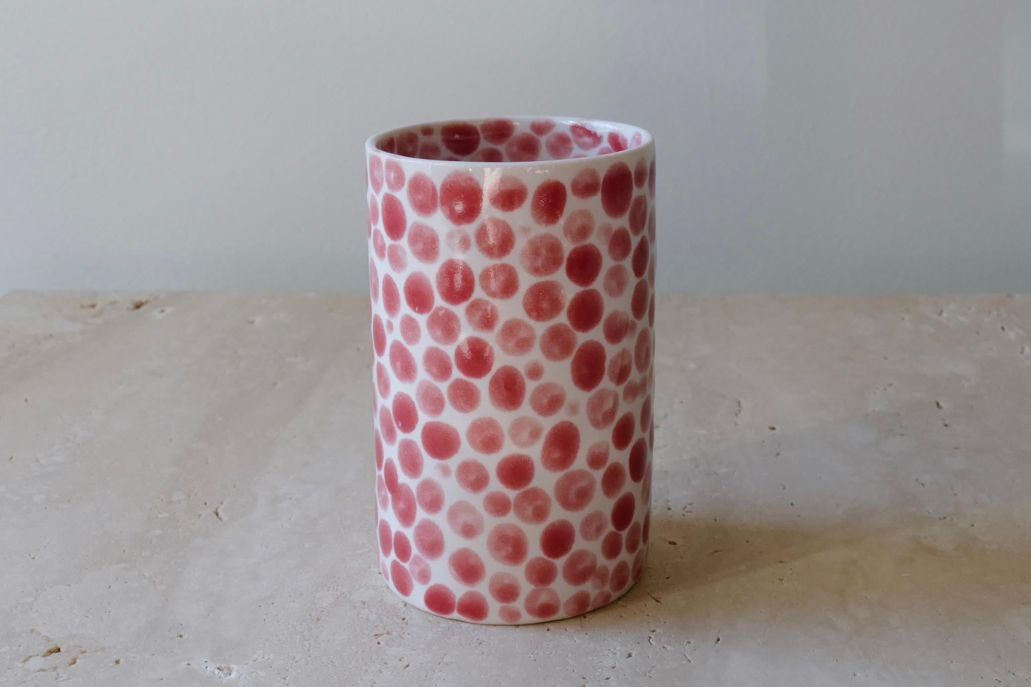 Ceramic drinking cup. Hand-cast in porcelain and once bisque fired, each dot is hand-painted with a shiny red glaze. An unconventional layered glazing technique, developed by the artist, is used in these cast porcelain pieces. The straight walls and