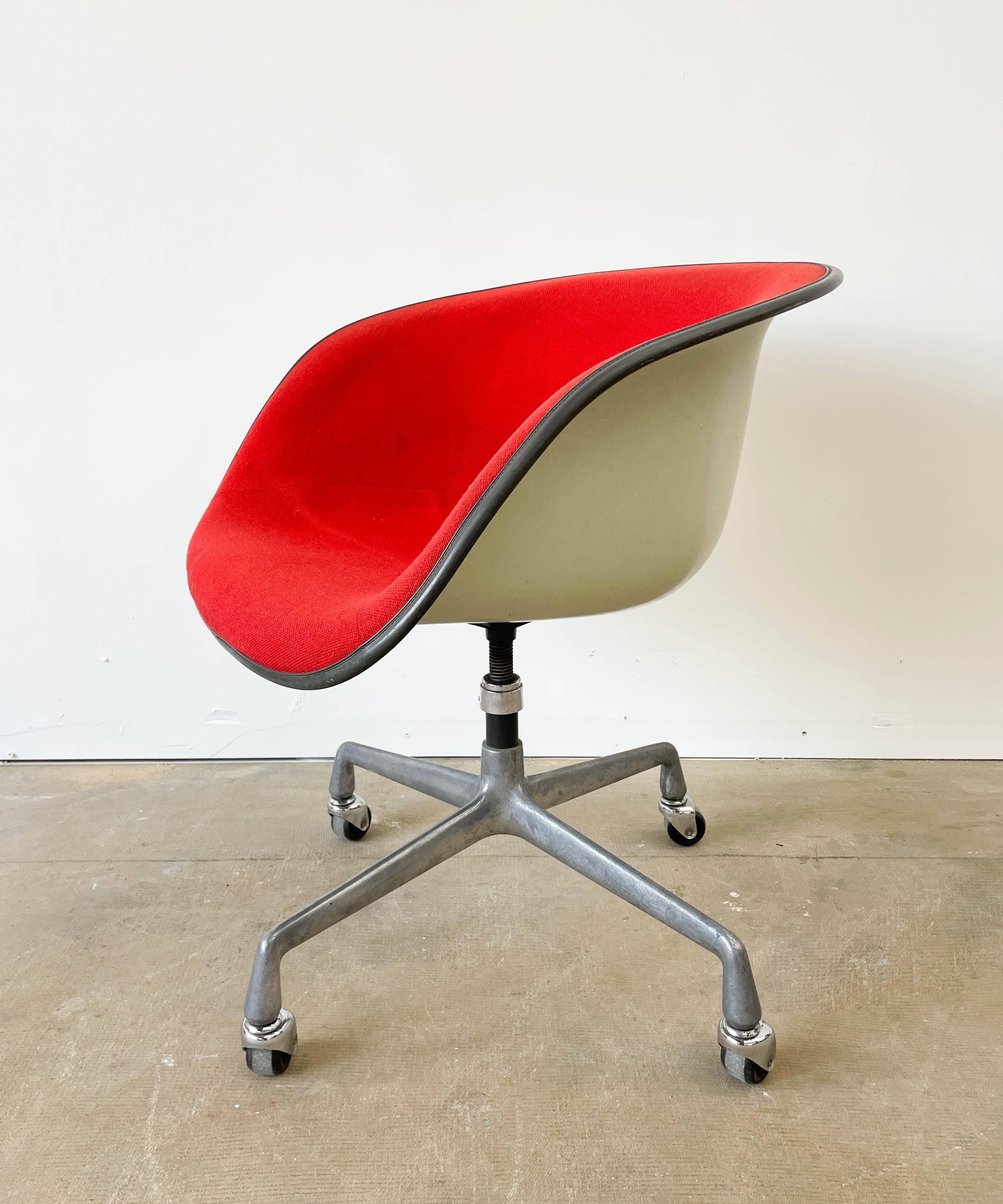 A 1961 piece from Herman Miller, this Eames-designed low-back armchair sits on a swivel and caster base. The piece is made from fiberglass, steel, and bold red fabric. There are minimal stains visible on the fabric, which is original from the 1960s.
