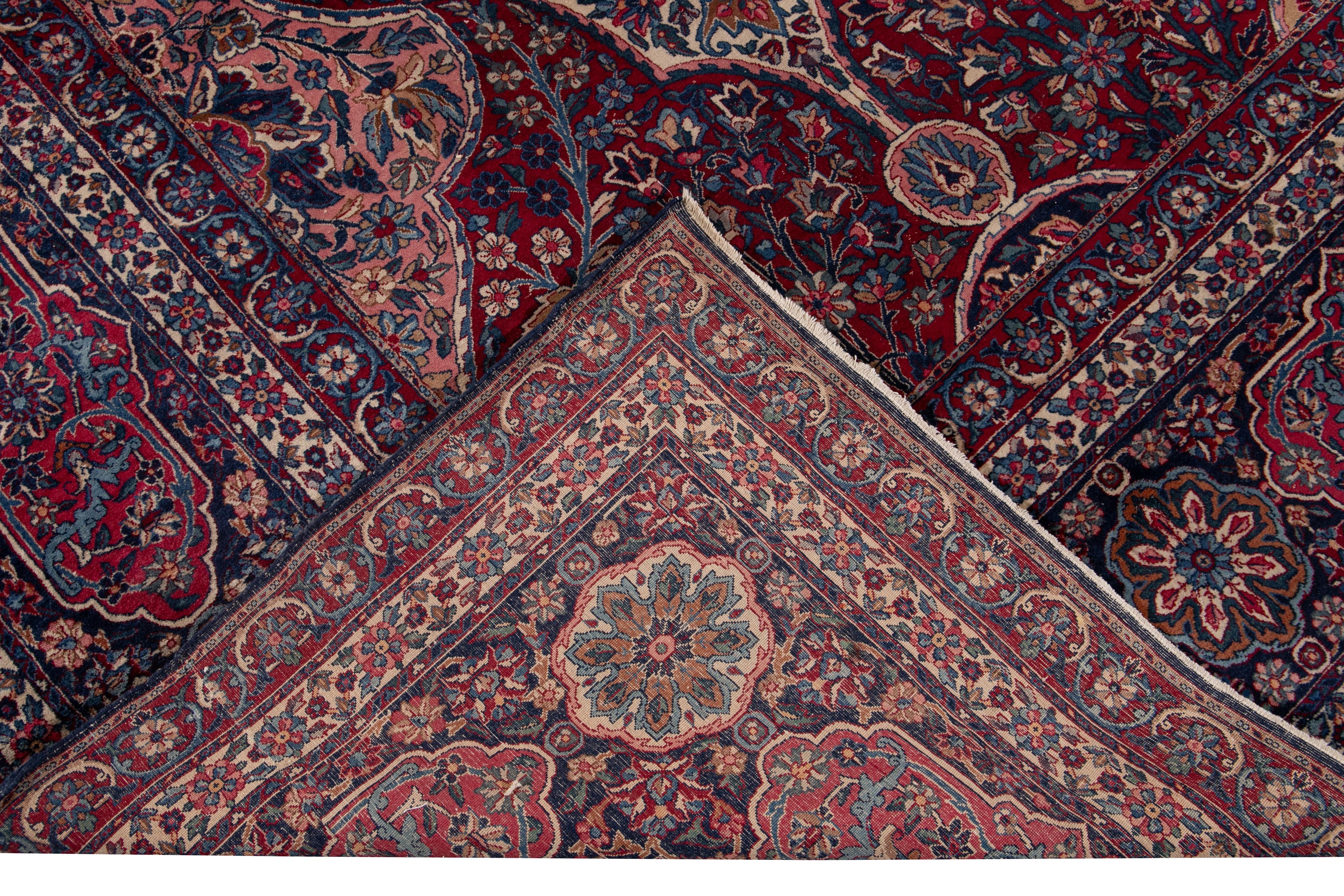 Beautiful antique oversize Kerman hand knotted wool rug with a red field. This Kerman rug has a navy-blue frame and multi-color accents in a gorgeous all-over multi-medallion Botanical floral design. 

This rug measures: 11'8