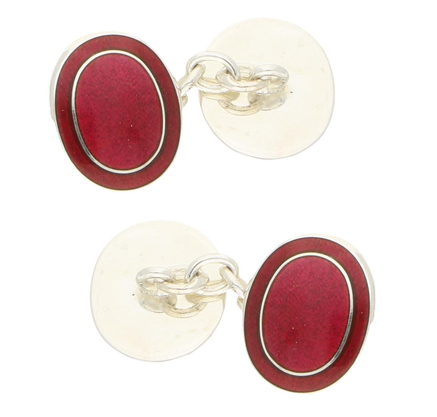 A pair of enamel oval cufflinks in sterling silver. 
Each cufflink is designed as two oval sterling silver plaques decorated with red enamel within a frame of darker red enamel, the plaques connected with a belcher link chain. Dimensions: 1.7x1.4cm.