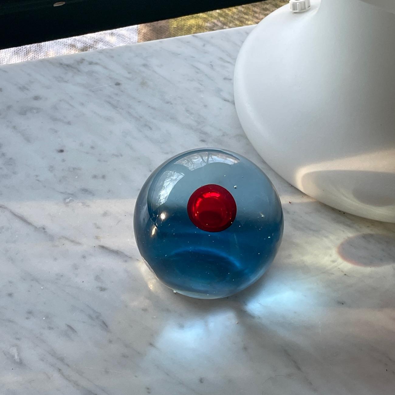 Un design meraviglioso e minimalista che ricorda i cubi in vetro artistico di Caliari Venini Inciso.  

Questo ha una sfera rossa all'interno di una sfera più grande di colore azzurro e chiaro.  Conserva sia il marchio 