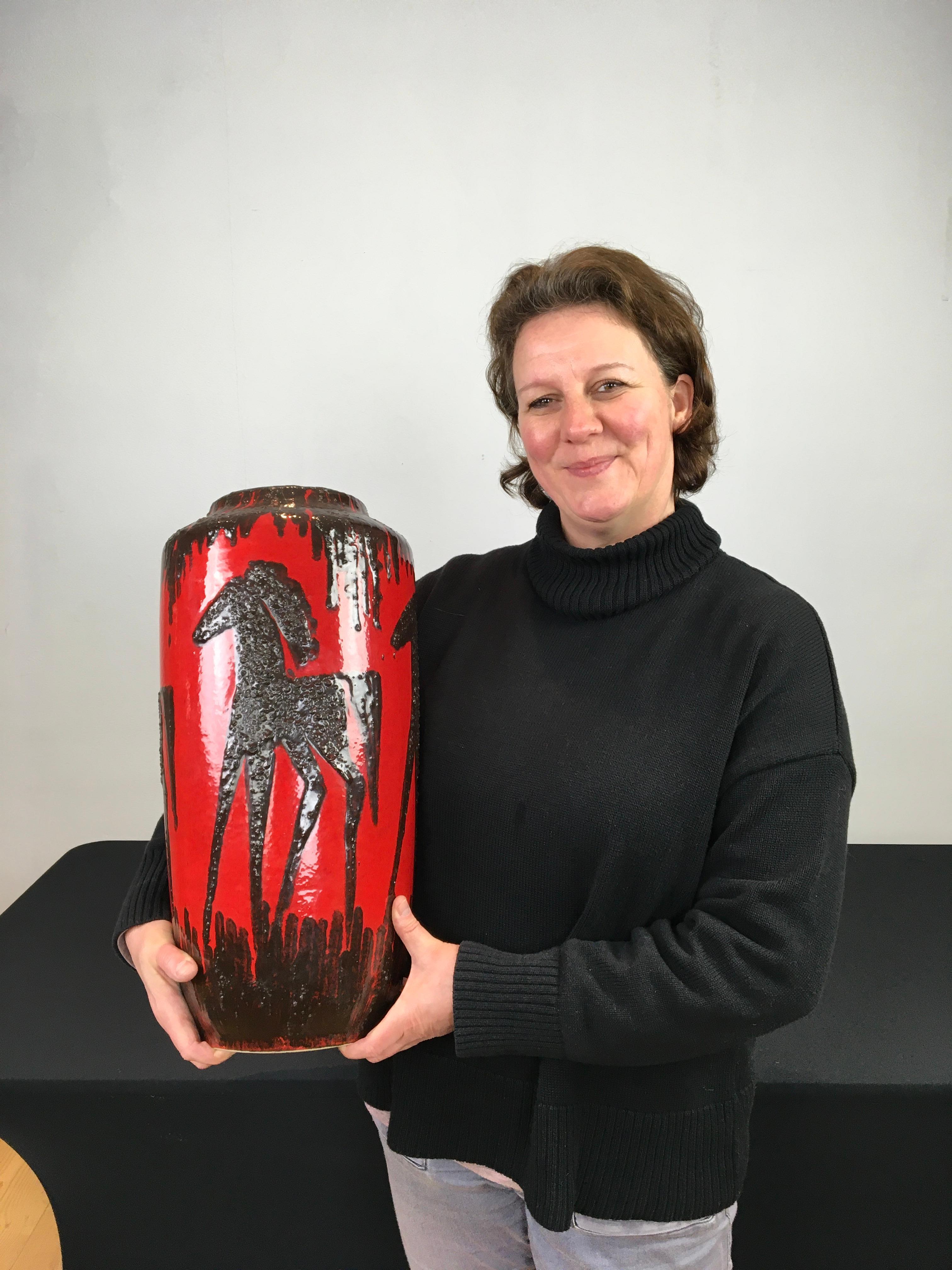 Vase en lave grasse rouge des années 1960 avec des chevaux.
Vase en poterie d'art de l'Allemagne de l'Ouest par Scheurich 
est de couleur rouge avec des chevaux marron foncé ou noirs.
Le motif est embossé ou en relief sur ce vase rouge