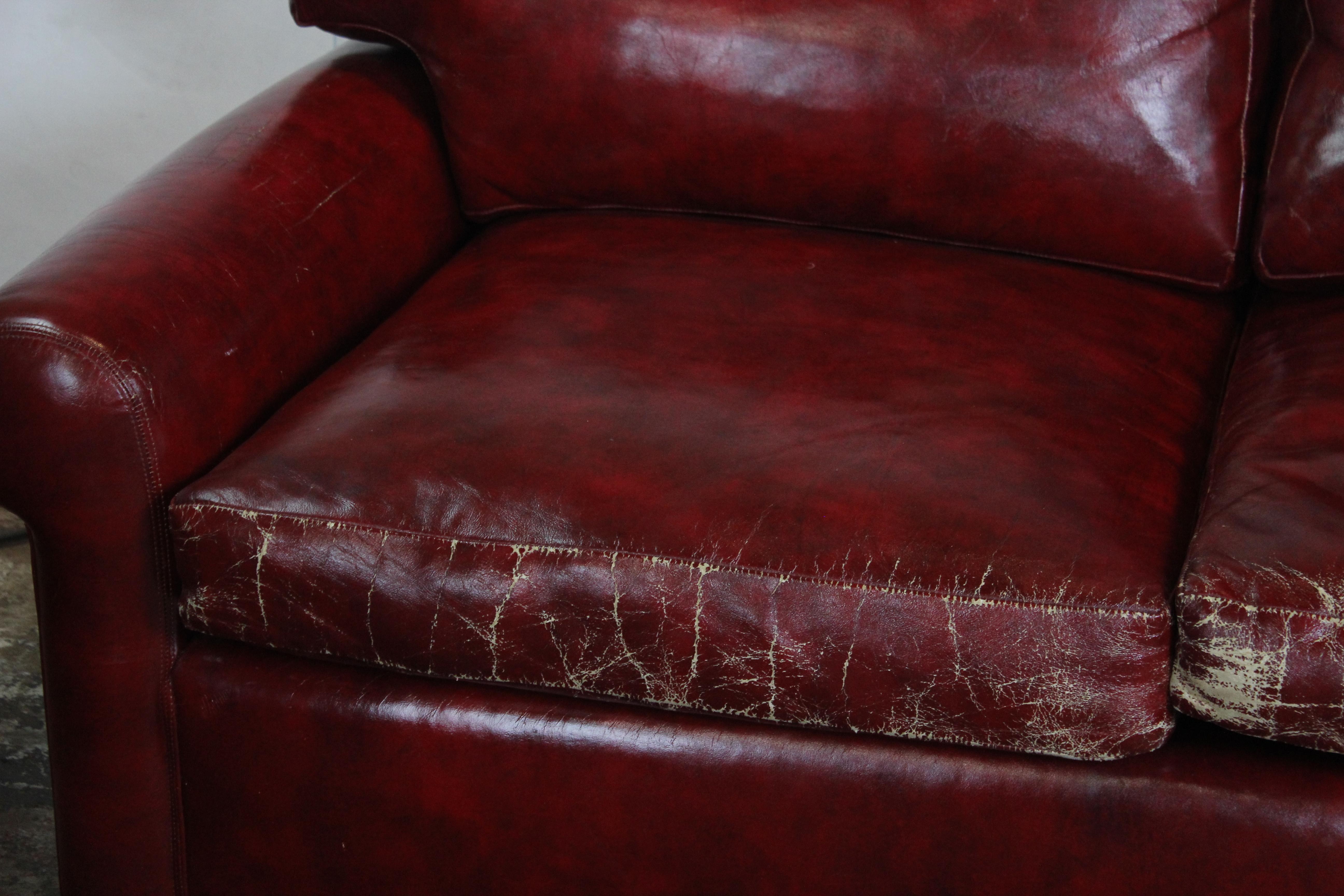 Red faux-leather loveseat. The seat cushions are down fill and standing on four castors.