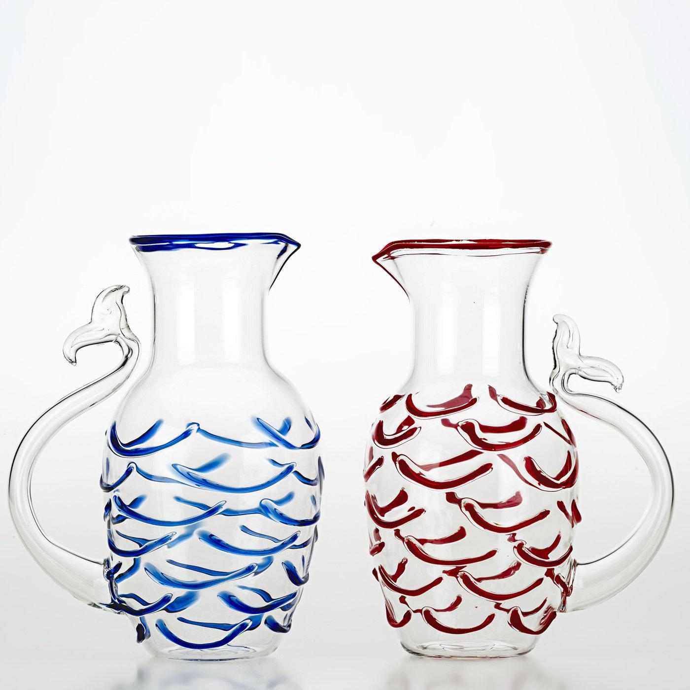 This jug was inspired by the majestic world of the sea. Its body is reminiscent of the sinuous forms of a fish and its curving handle takes the shape of a fish tail. The transparent vessel is covered in a textured scale pattern in glass with a