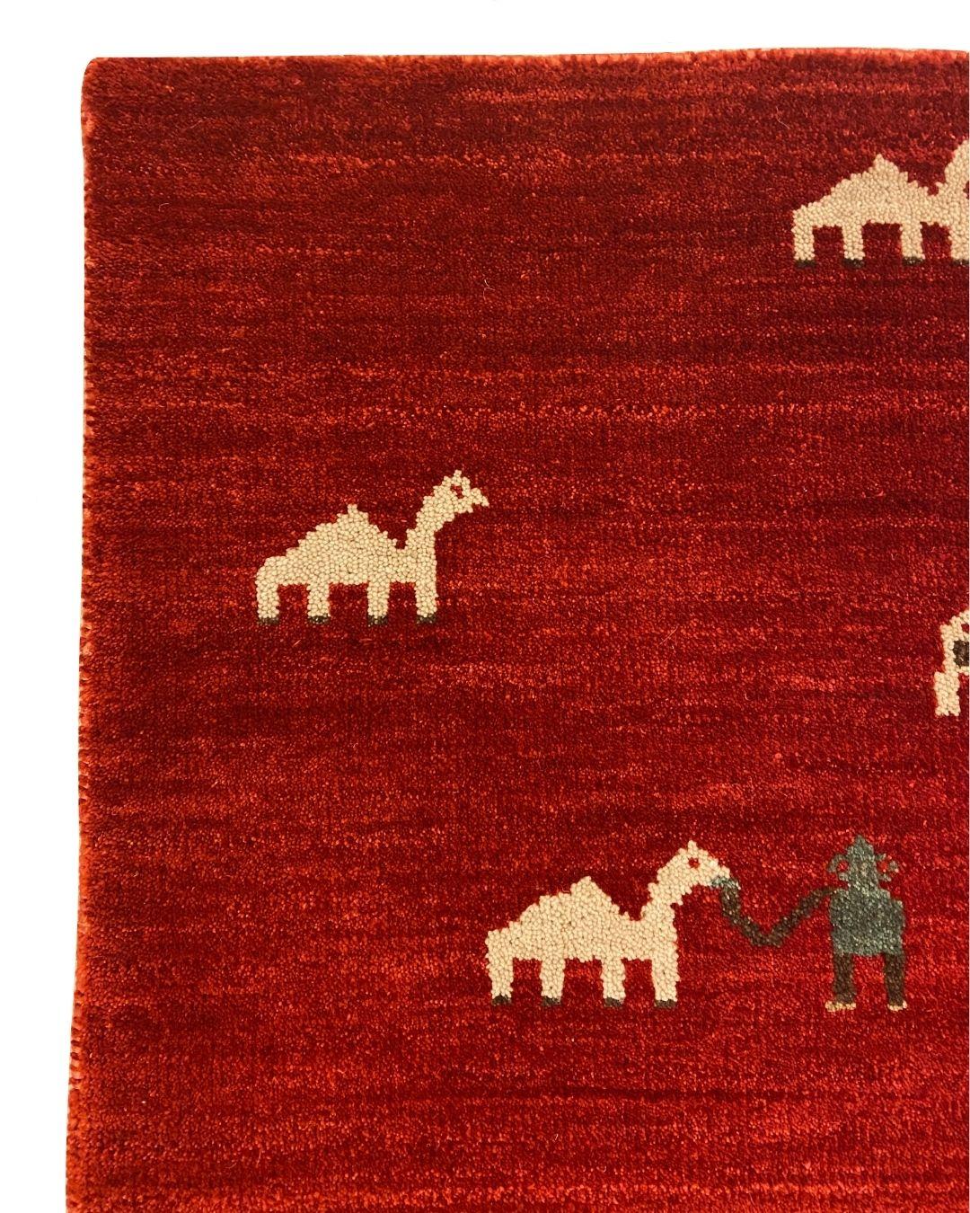 Dieser rote Gabbeh-Teppich mit den Maßen 2' x 3' zeigt eine lebendige Sammlung von Tier- und Menschenfiguren in Grün, Creme und Braun, die eine einzigartige und lebendige Darstellung des ländlichen Lebens bieten. Das Design enthält eine Mischung aus