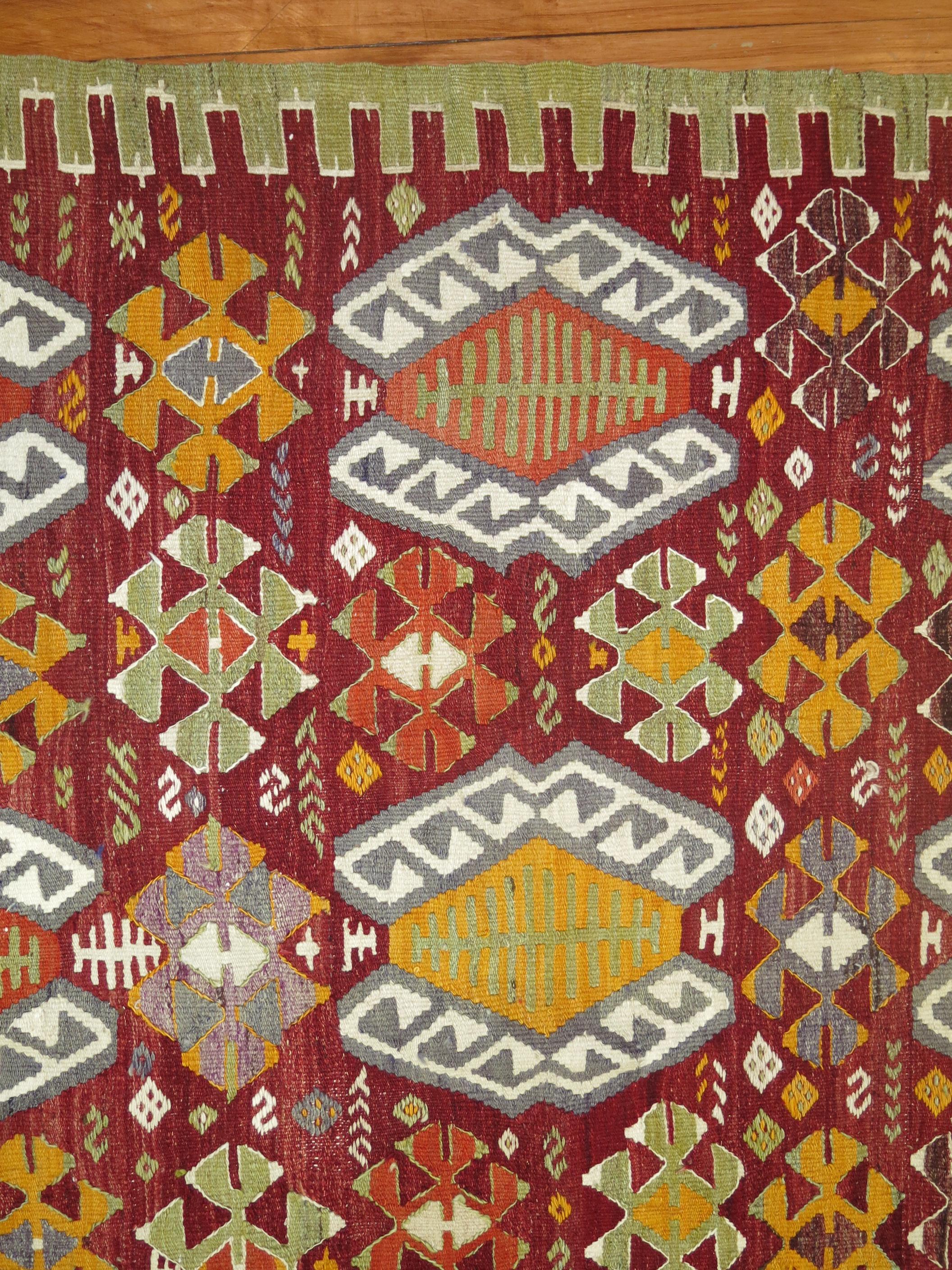 Vintage Turkish Kilim with a colorful repetitive geometric design on a vivid red colored ground.