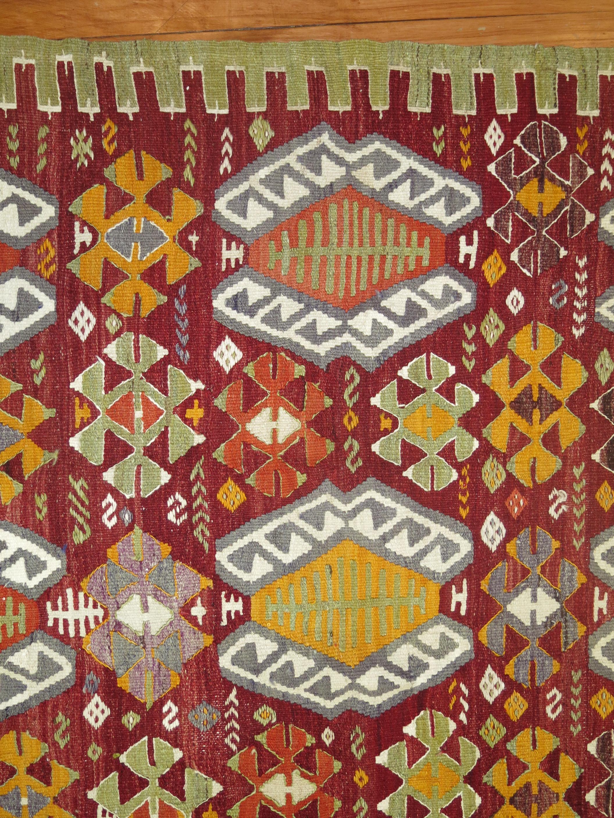 Türkischer Kelim im Vintage-Stil mit einem farbenfrohen, sich wiederholenden geometrischen Muster auf einem leuchtend roten Grund.