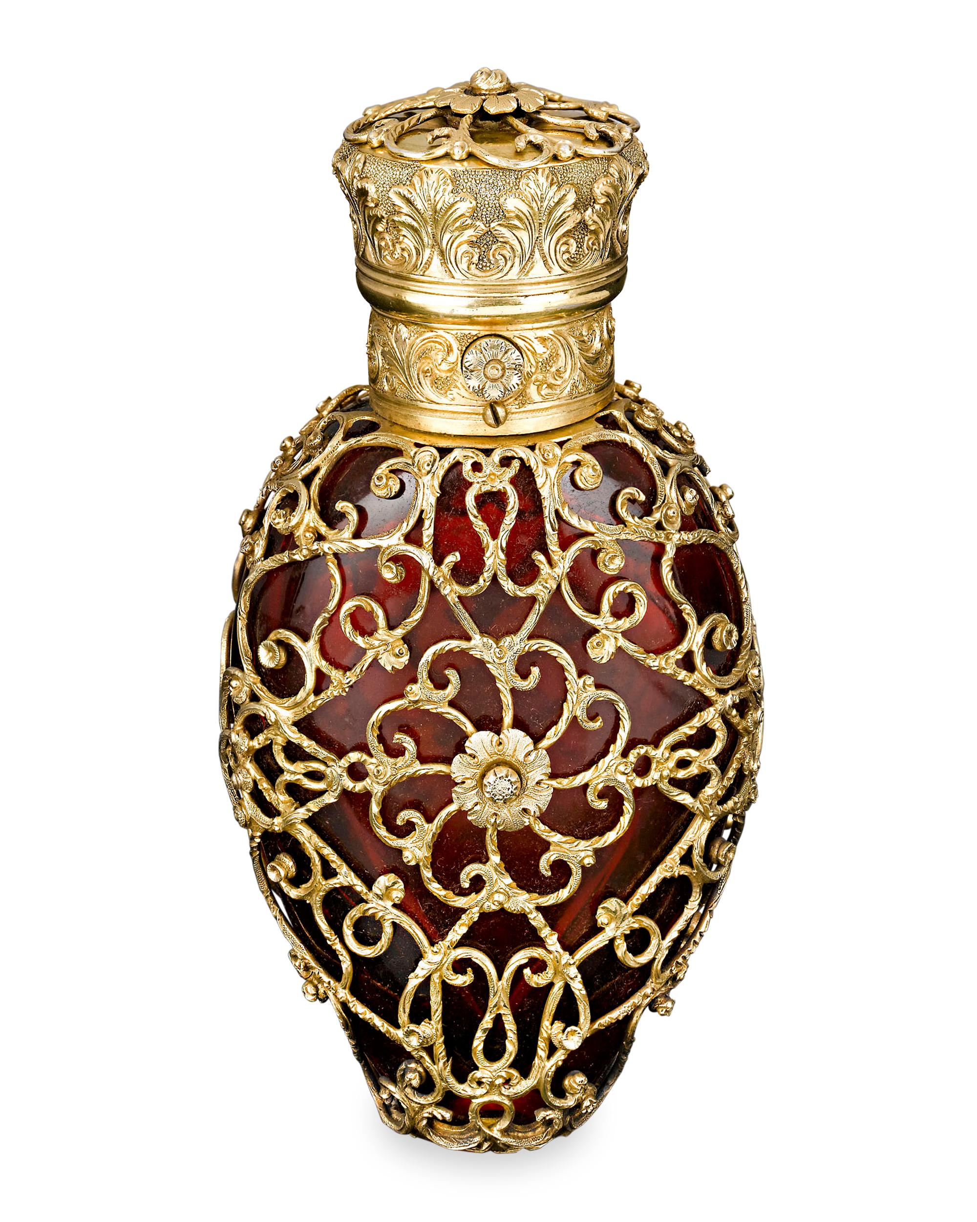 Incredible silver gilt pierced work envelopes this red glass perfume bottle by London glass artisan Thomas Robert Mellish. The spring-open lid of this elegant perfume is activated with the push of a button and features a most intricately chased