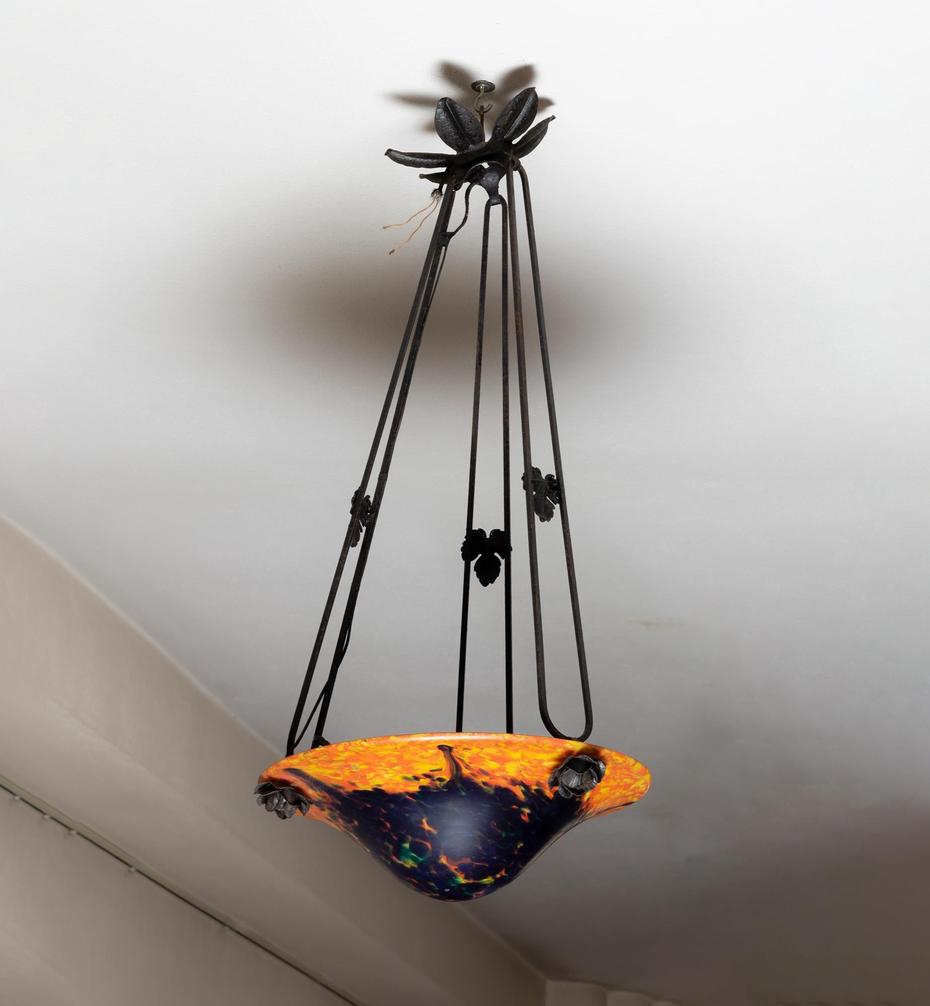 Esta lámpara de techo francesa Art Nouveau de principios del siglo XX presenta un cuenco de vidrio moteado rojo y azulado al estilo del cristal de Nancy, montado sobre un marco de hierro forjado con motivos florales decorativos.

El vidrio presenta