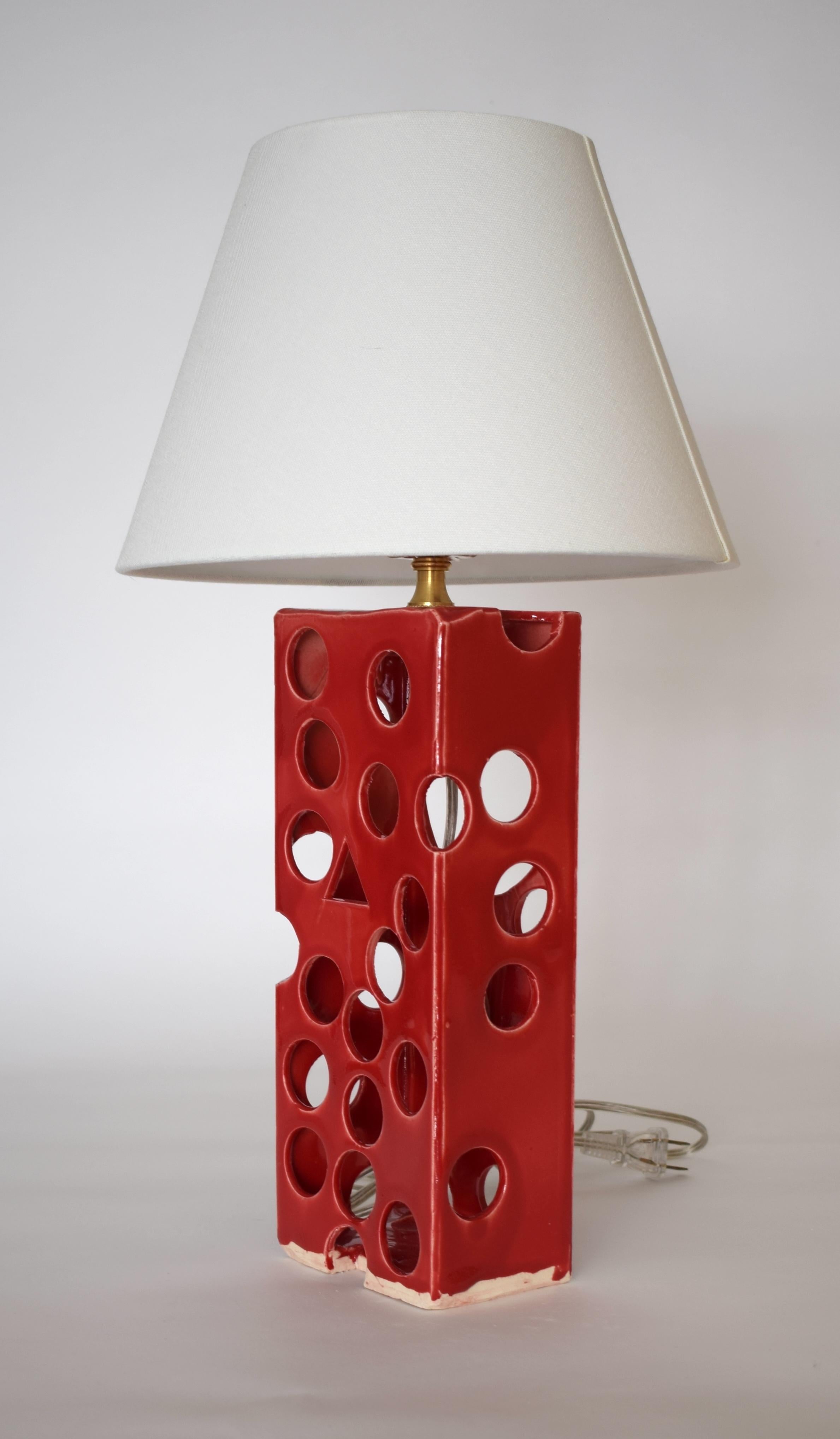 Crafted with precision and sophistication, this one-of-a-kind piece features a rectangular clay prism adorned with a random array of circular openings. This version shown is glazed red (Fabio) and Illuminated by both E26 socket and interior LEDs.