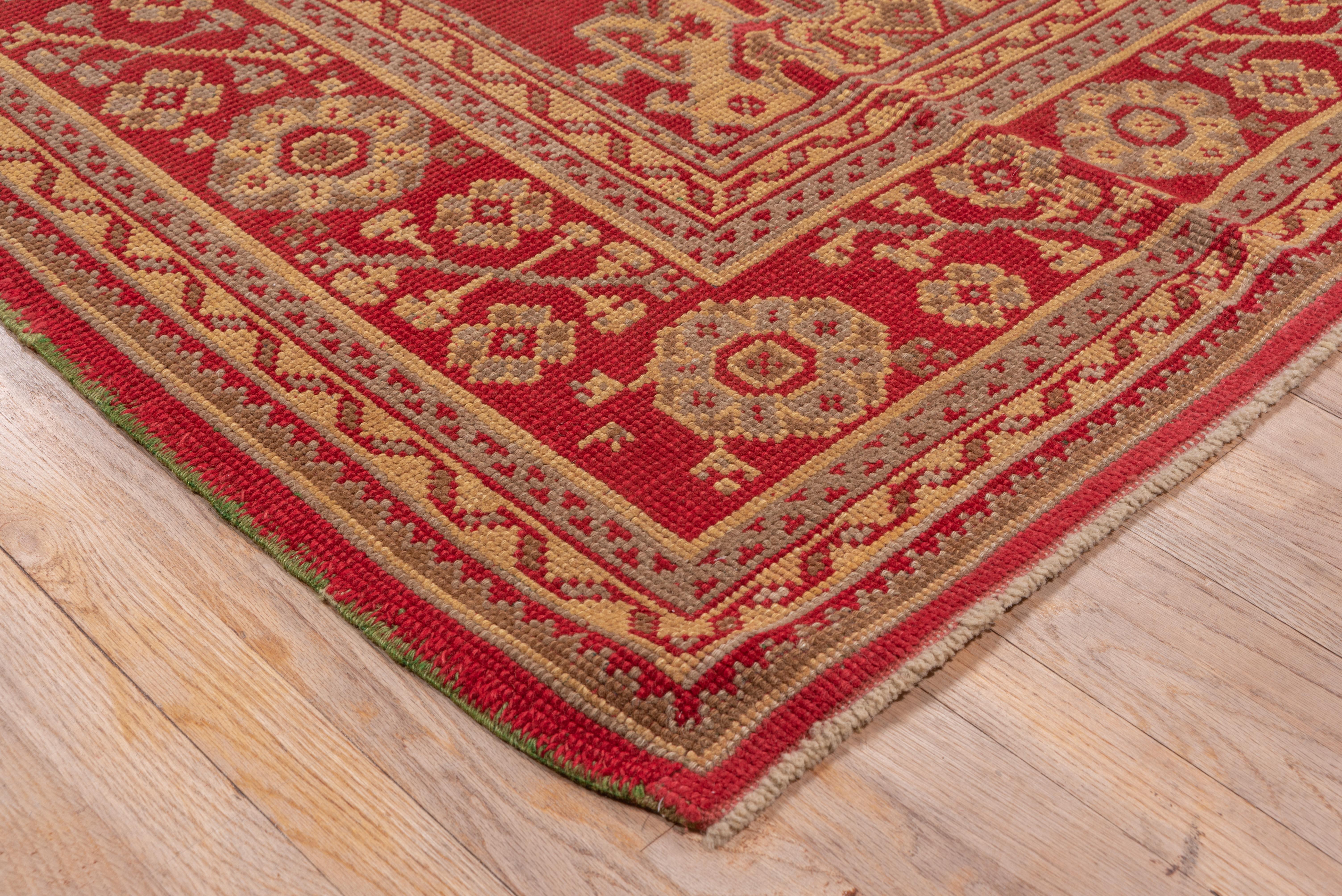 The Turkey red field of this Smyrna-style carpet displays three alternating columns of ragged palmettes and diamond-shaped Yaprak (leaf) medallions accented with botehs. The matching red border shows rosettes and hyacinth sprays in the Ottoman