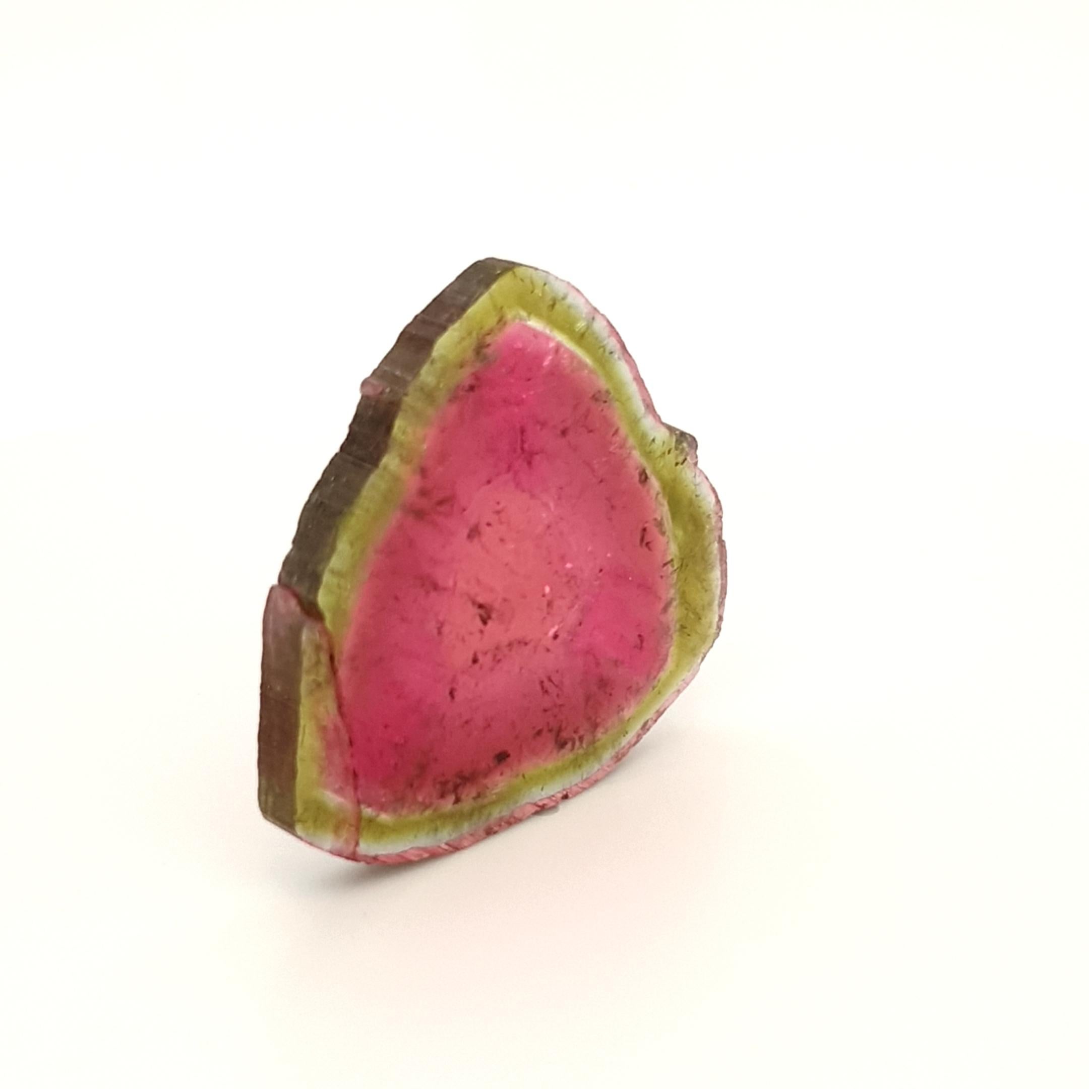 The tourmaline slice shows a typical pattern for a tourmaline watermelon from Brazil.
The core goes from pink to intense pink to a green outer band. 
nicely banded, have precise transitions and well saturated colour.
The noble quality of this piece