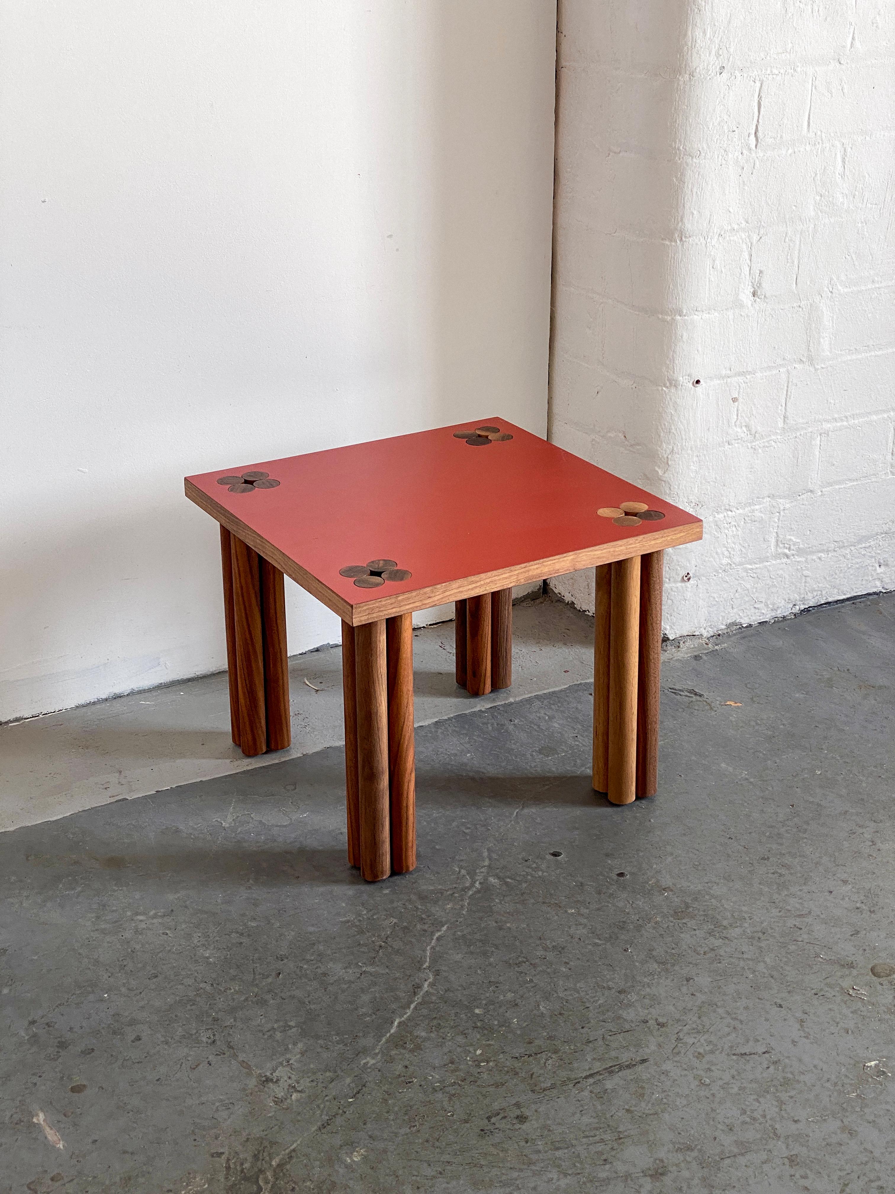 Red Hana side table by Tino Seubert.
Dimensions: D 43 x W 38 x H 50 cm. 
Materials: Solid walnut wood, walnut veneer, Formica.
Oak or other wood possible. 

Tino Seubert
When he first made his now signature wicker and aluminium stools and benches in
