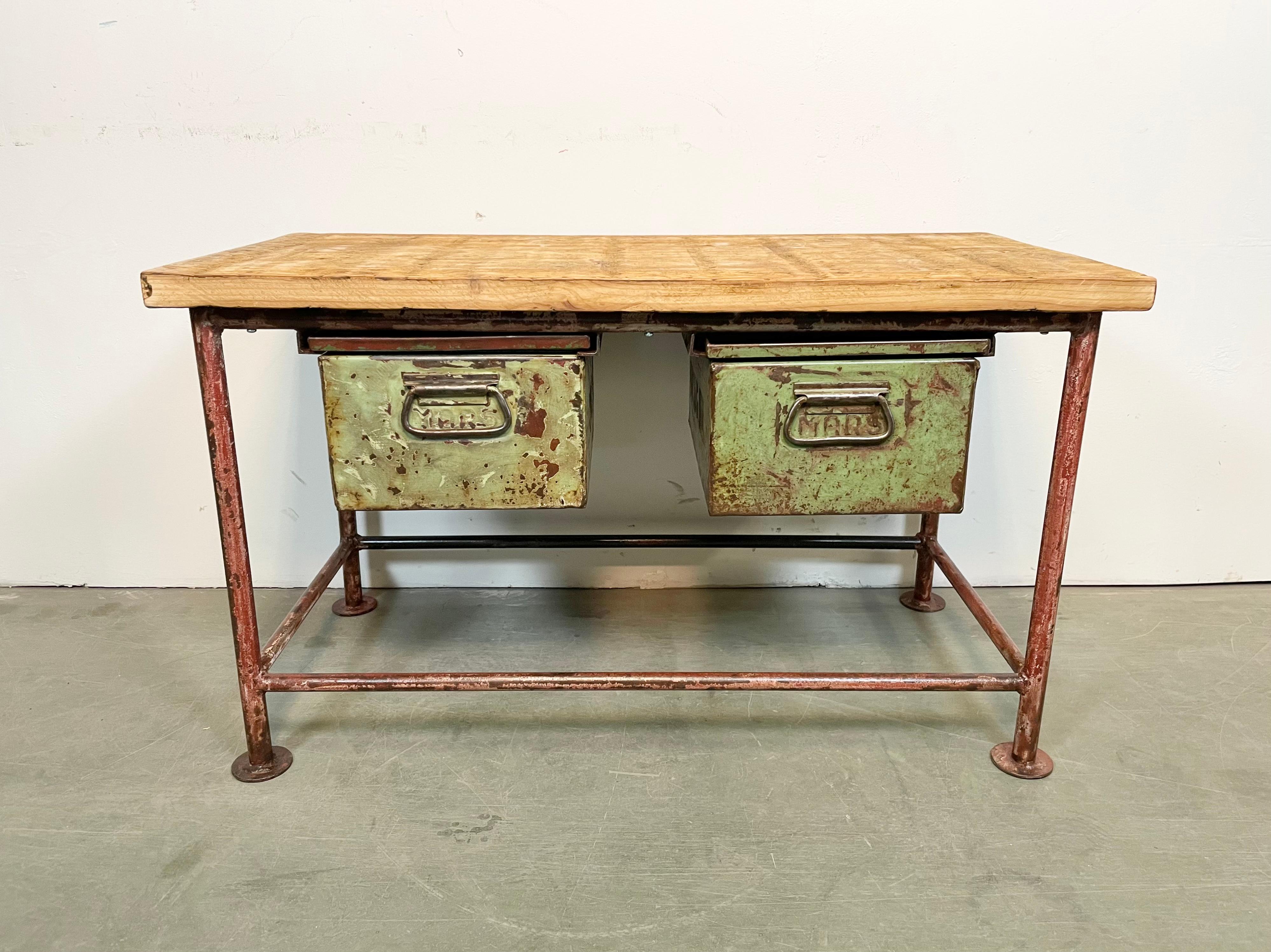Tavolo da lavoro industriale vintage degli anni '60. Presenta una struttura in ferro rosso, un piatto in legno massiccio e due cassetti in ferro verde. Peso: 34 kg.