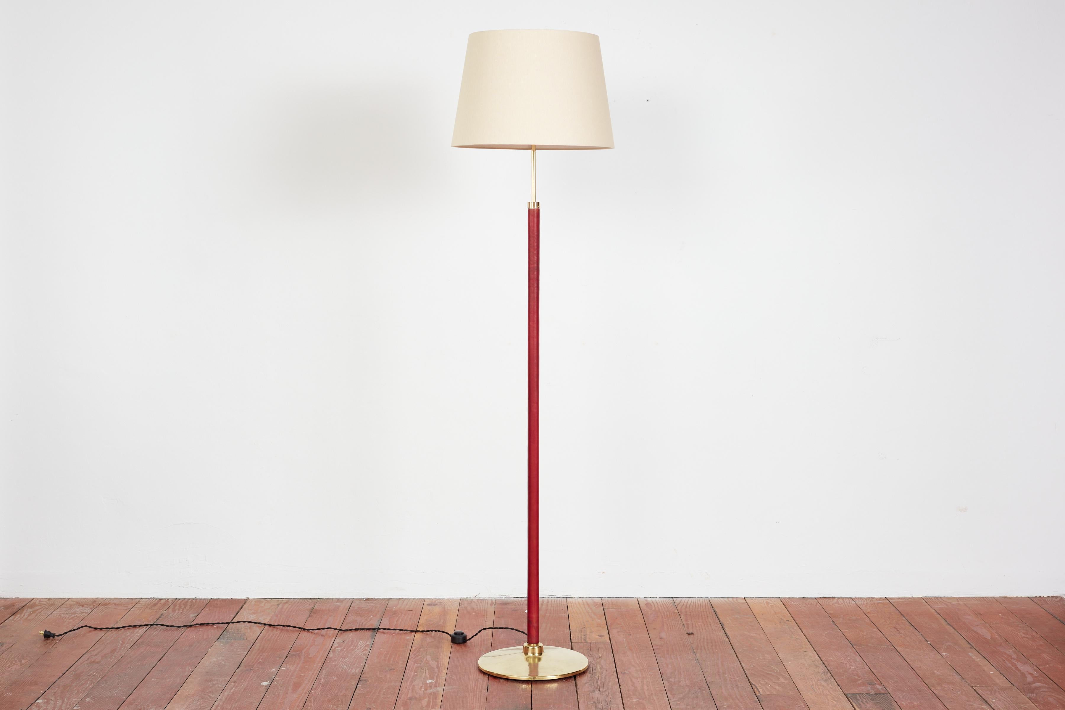 Handsome French floor lamp by Jacques Adnet.

Signature hand-stitched oxblood leather, contrast stitching, with circular brass base and new silk shade. 

Newly rewired. 