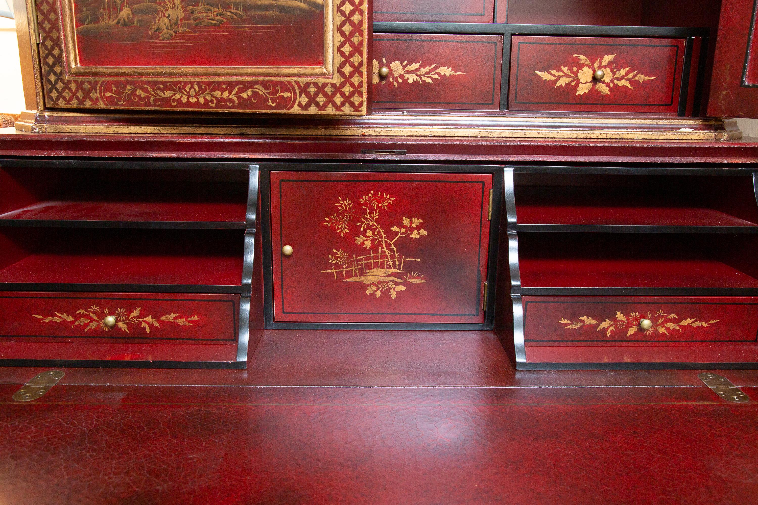 This is a highly decorative and stylish Chinese red painted bureau bookcase decorated overall with gilt chinoiseries. The top section contains a broken arched pediment over two conforming doors. The bottom section contains a drop-front writing