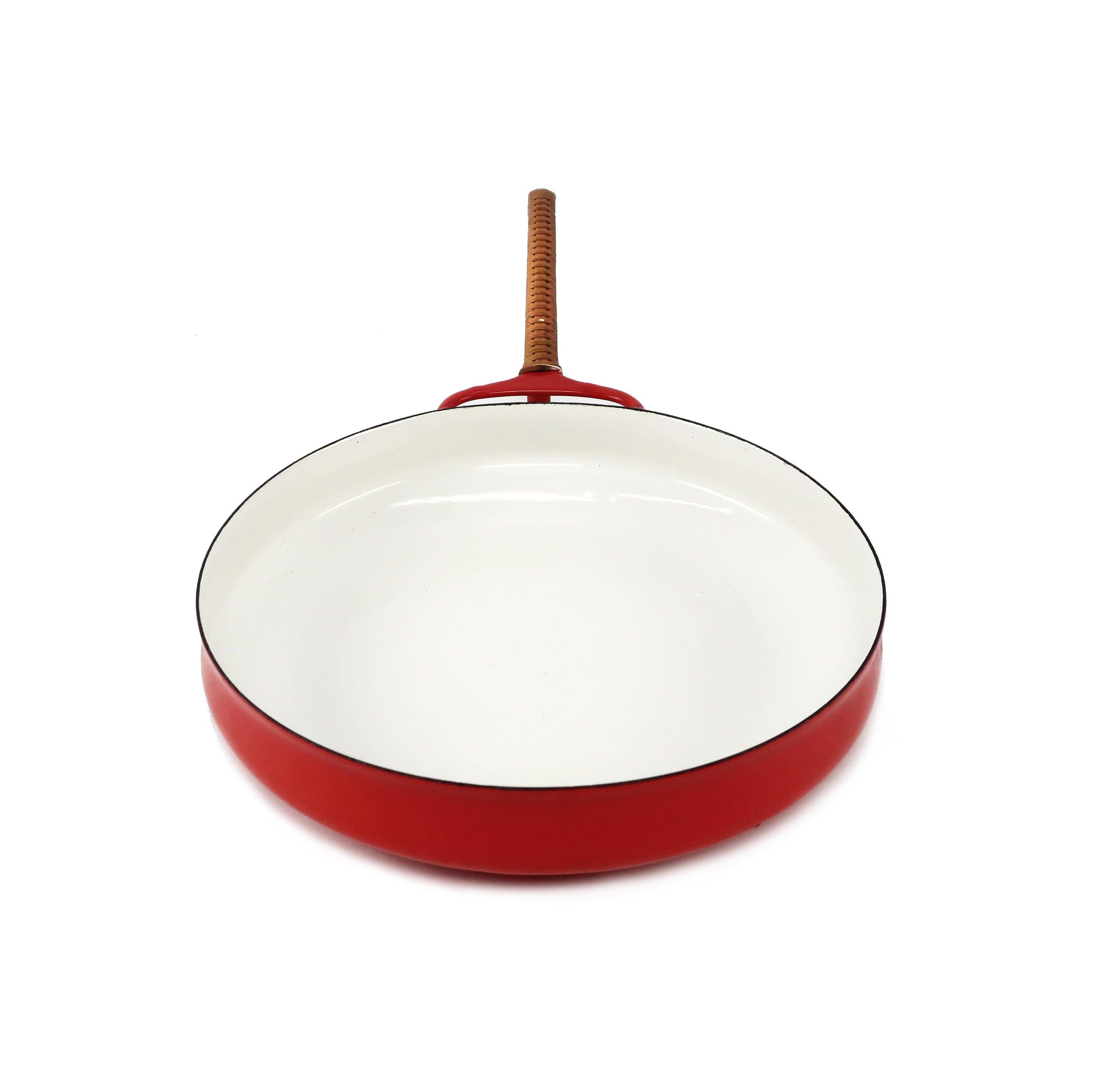 A Danish modern Classic, this red Kobenstyle skillet/saute pan designed by Jens Quistgaard for Dansk has red enamel on exterior, white interior enamel, and brown coated rattan wrapping on handle. The wrapping was only found on early pans and was
