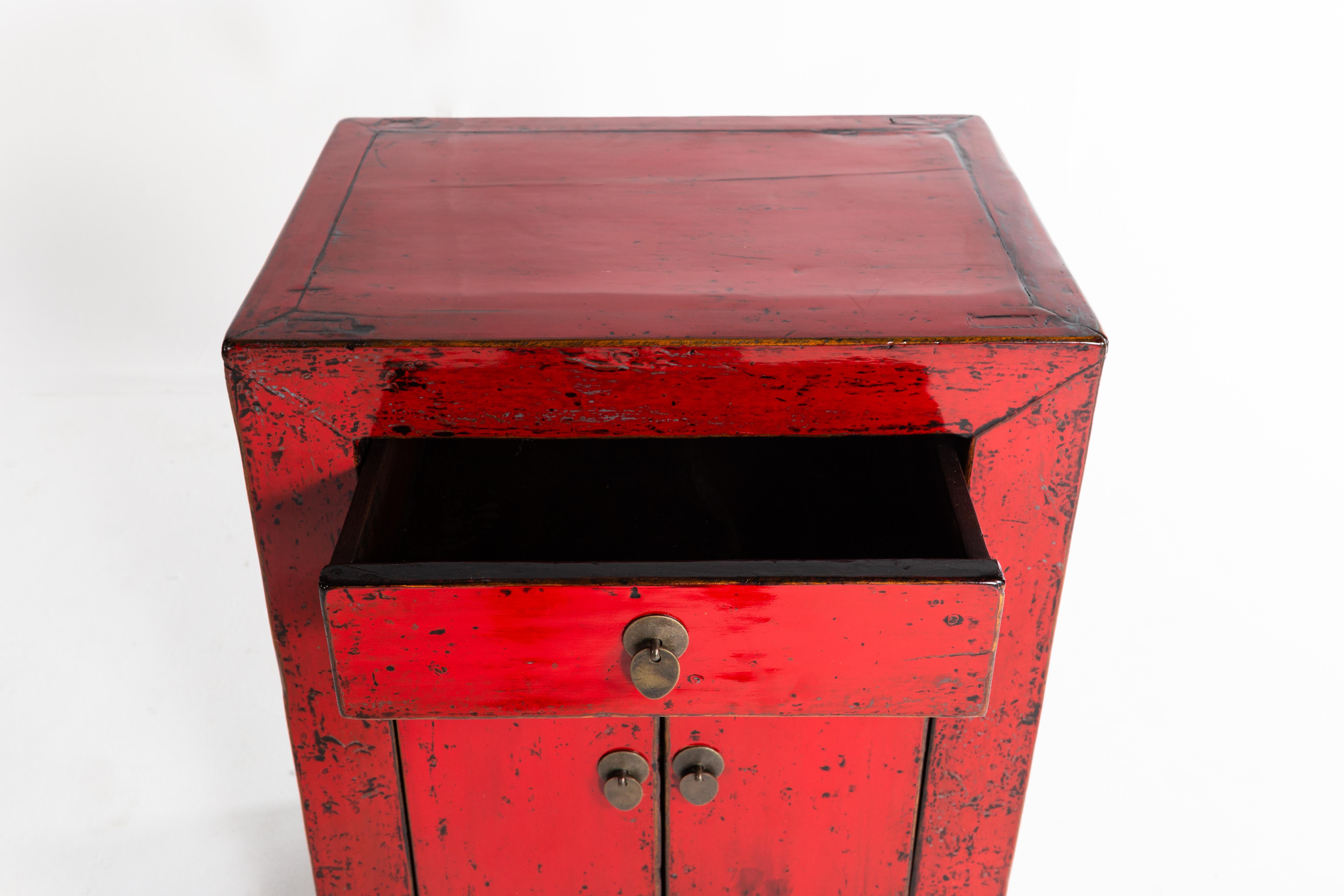 This red lacquer cabinet is from Shandong, China and was made from pine, elm, and lacquer, circa 1920. The piece features a pair of doors and a drawer for storage; wear consistent with age and use.