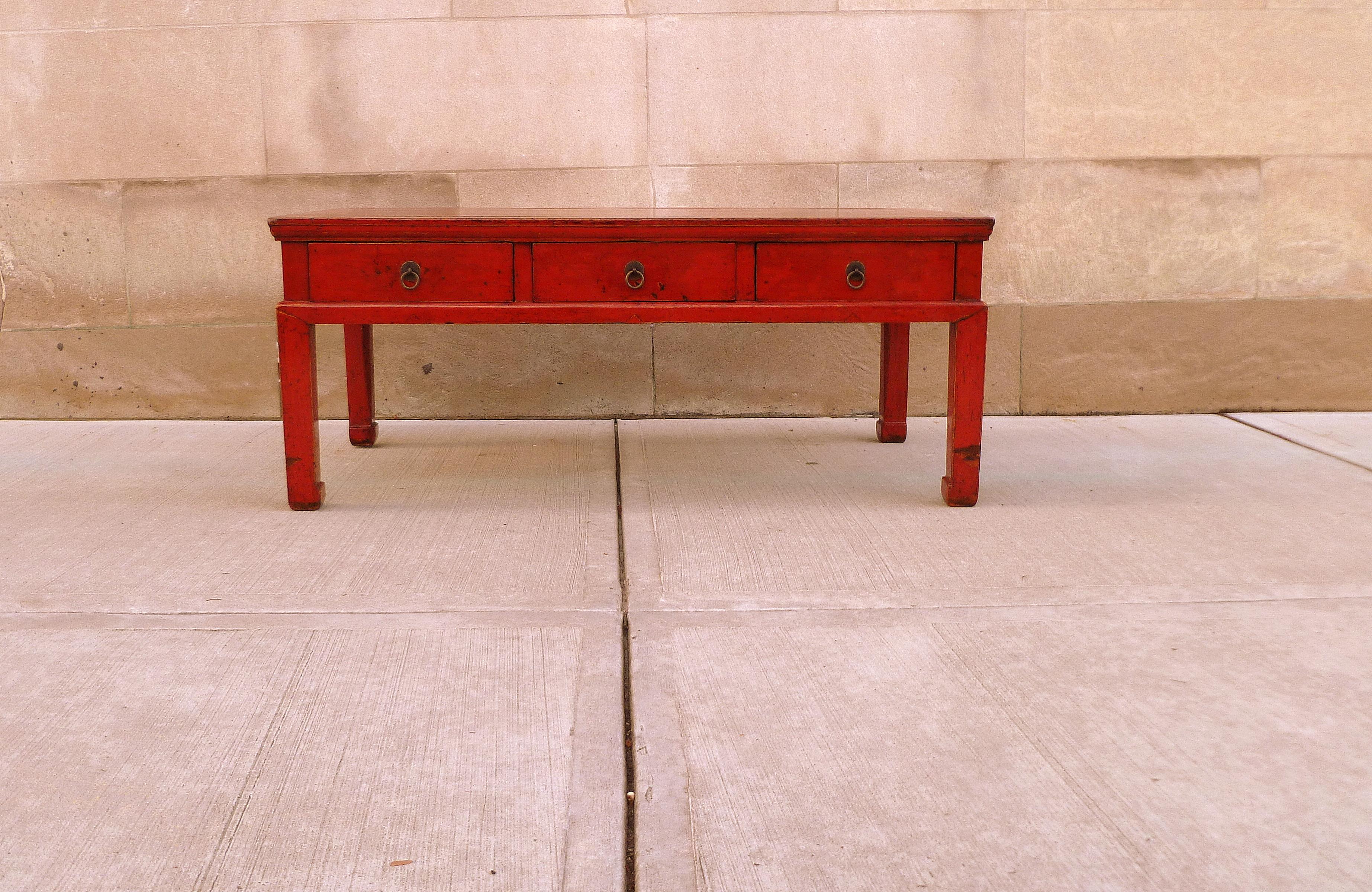 Antiques red lacquer low table with three drawers with brass pulls and straight legs with hoof feet.