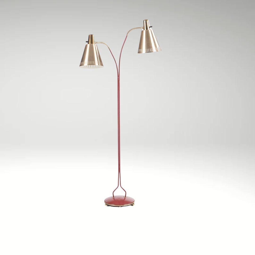 Una lampada da terra dal design accattivante, con una struttura in acciaio laccato rosso su una base circolare con dettagli in ottone. La lampada è dotata di due paralumi regolabili che consentono di personalizzare l'illuminazione. 
Altezza circa