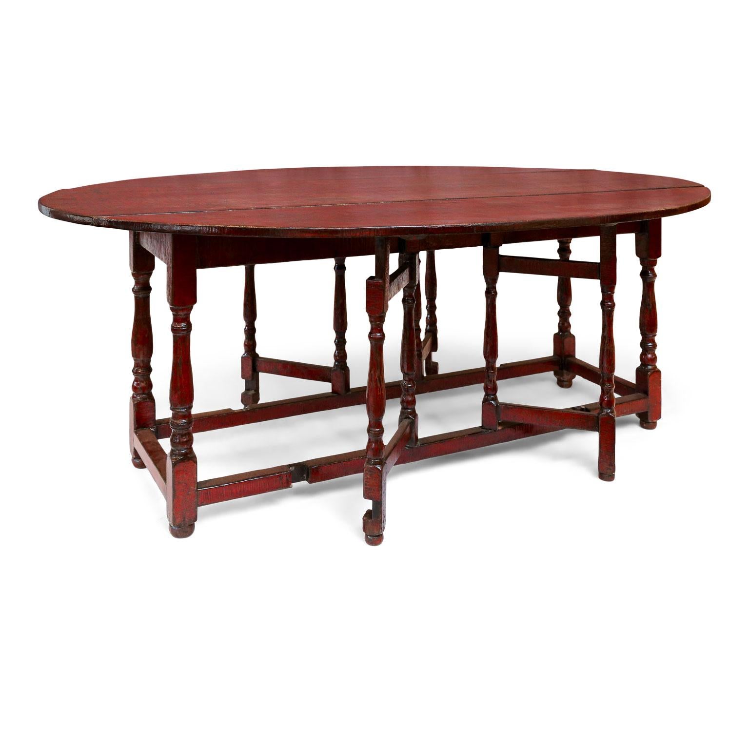 Red lacquered English table. Constructed circa 1950 using traditional methods – very sturdy. Oval shaped with leaves that drop transforming table into a wide demilune console or sofa table. Gate-leg base supports leaves. Untouched original red