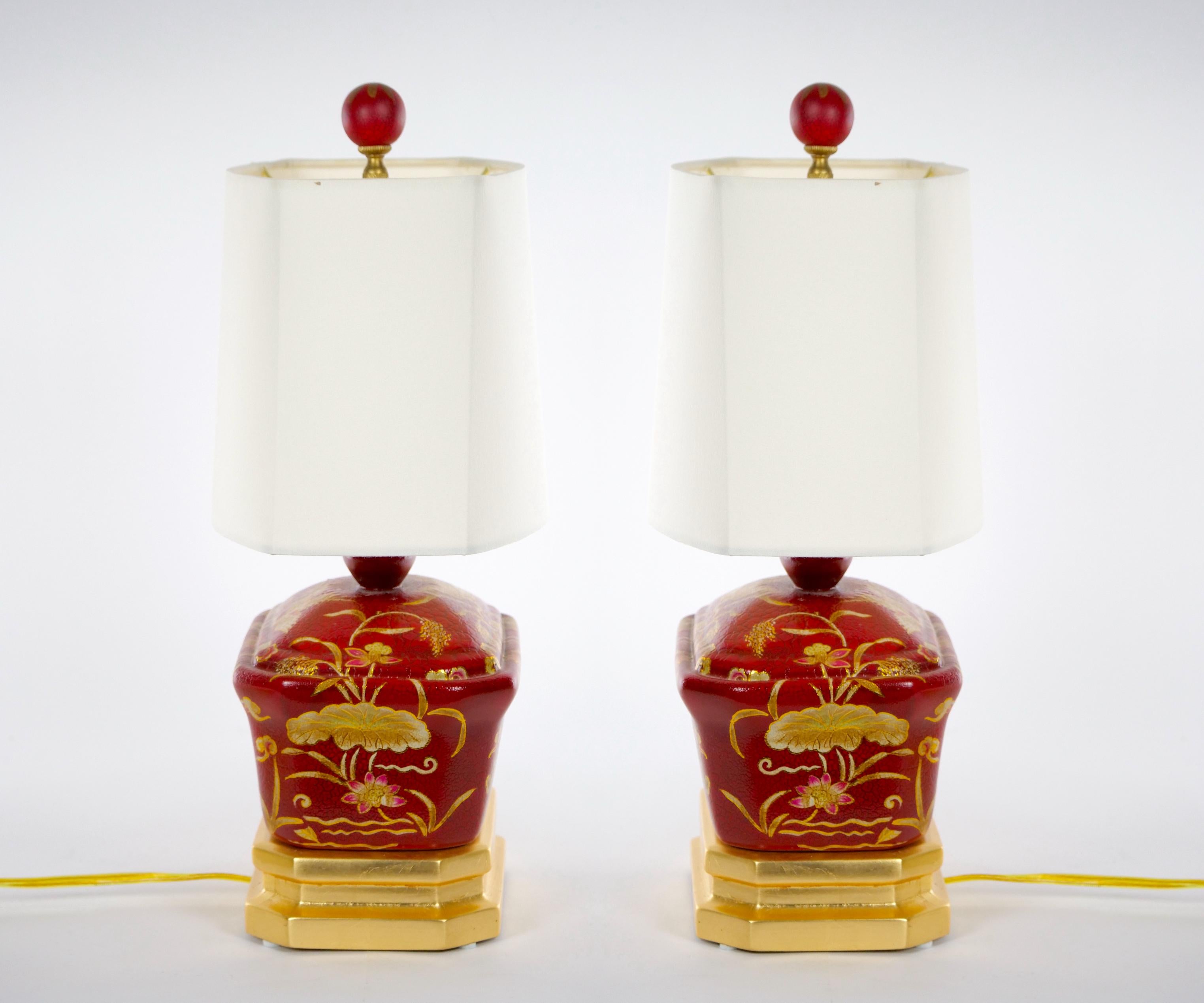 Beautifully hand painted and decorated red Lacquered chinoiserie scene details pair of small table lamp. Each lamp features a red lacquered decorated floral chinoiserie scene resting on an oval gilt wood base. Each lamp is in great working condition