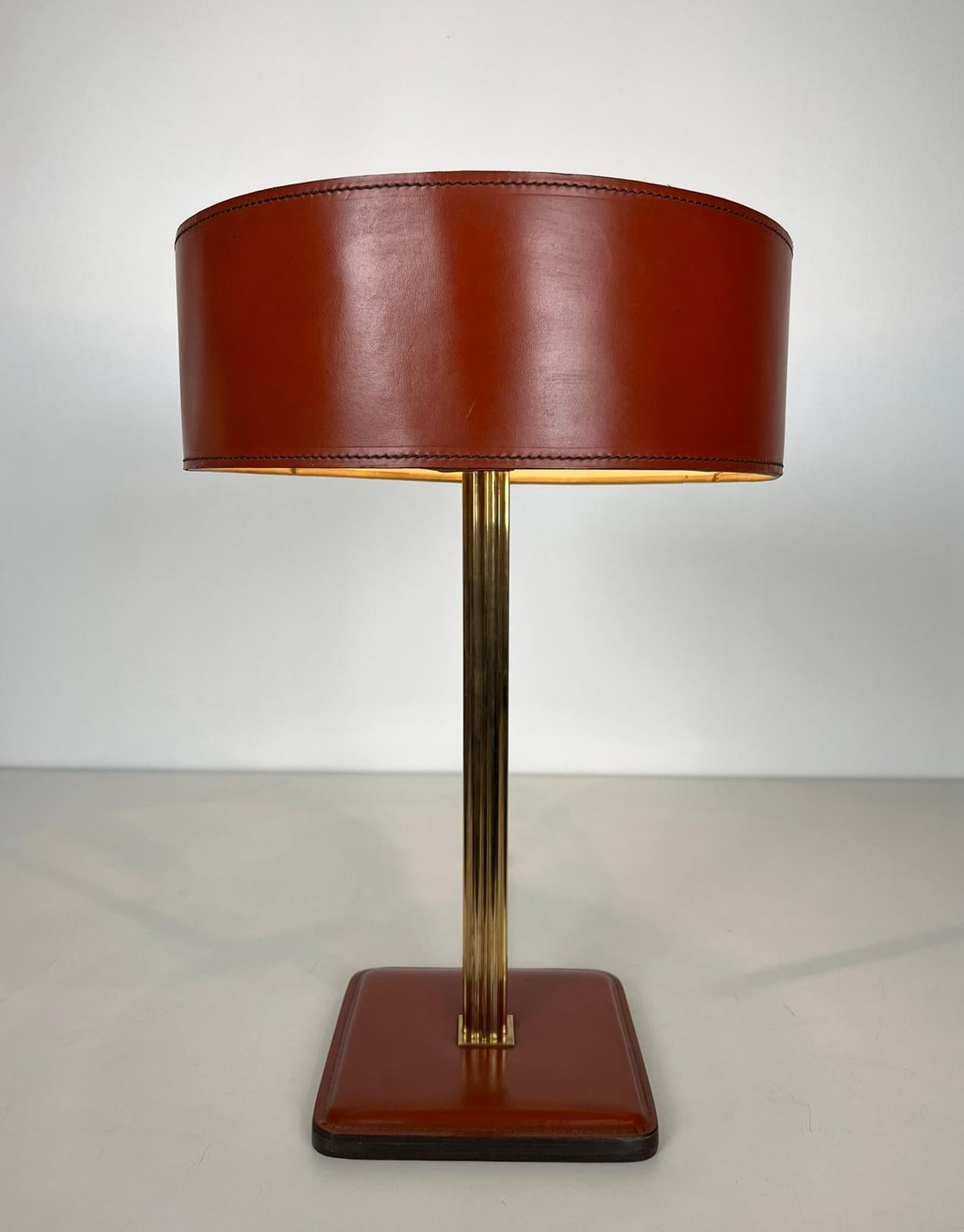 Cette lampe de bureau est fabriquée en cuir rouge et en laiton. Il s'agit d'une œuvre française dans le style de Jacques Adnet. Circa 1970