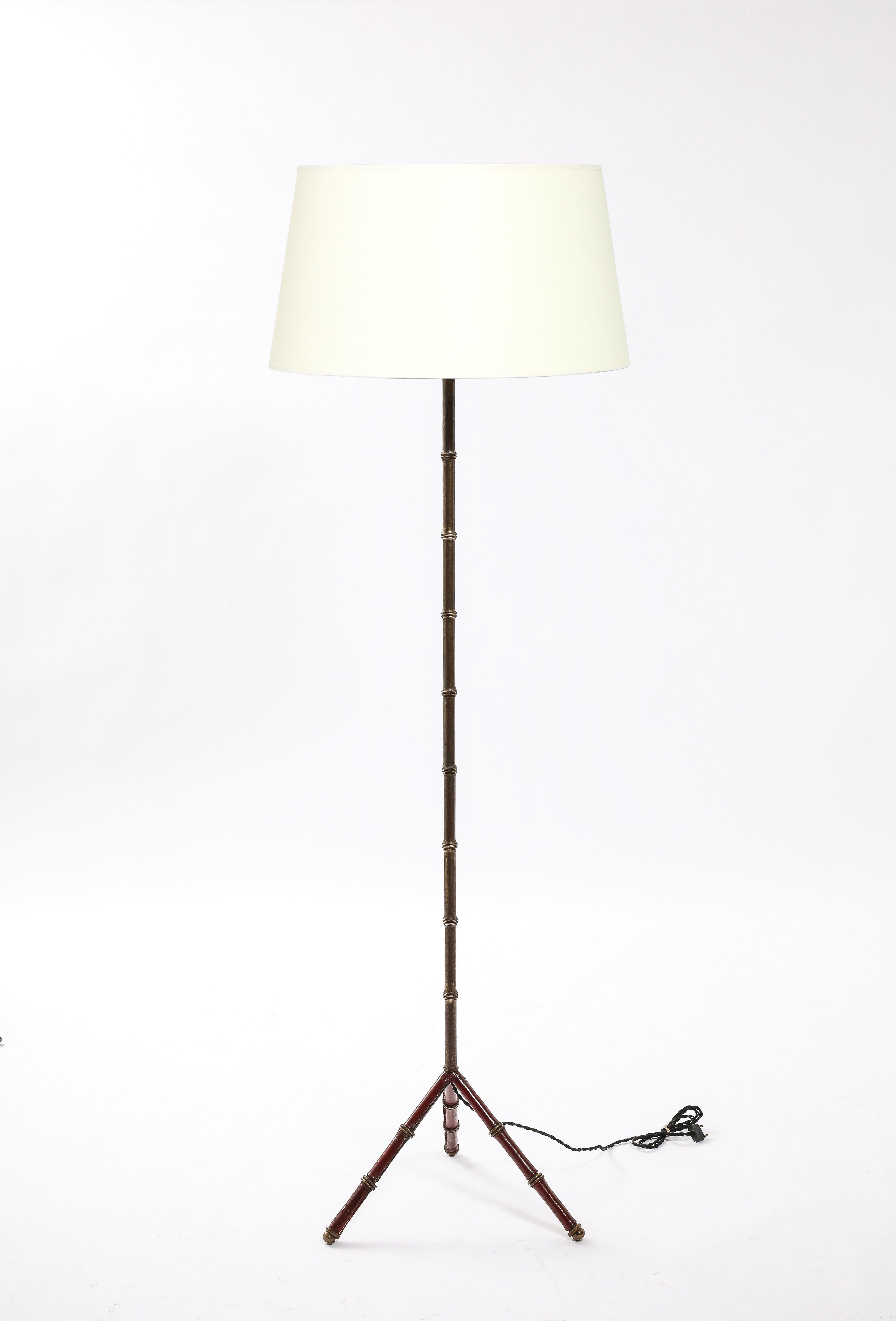 Tripod floor lamp in iron wrapped in red hand-stitched leather with a faux bamboo brass motif. 
