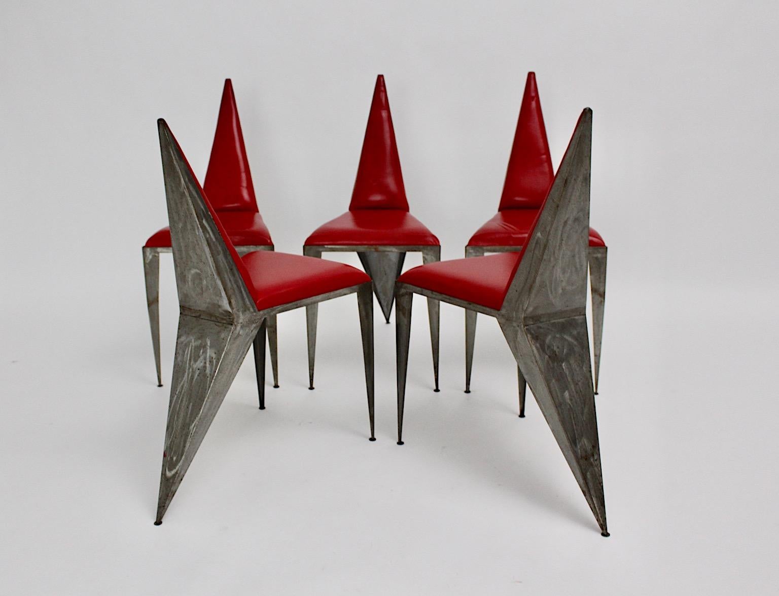 Un ensemble géométrique vintage en cuir rouge et fer de 5 chaises ou fauteuils de salle à manger, qui ont été conçus et exécutés en Autriche dans les années 1960.
Le cadre en fer brossé non traité, avec ses trois pieds et son siège arrière pointu,