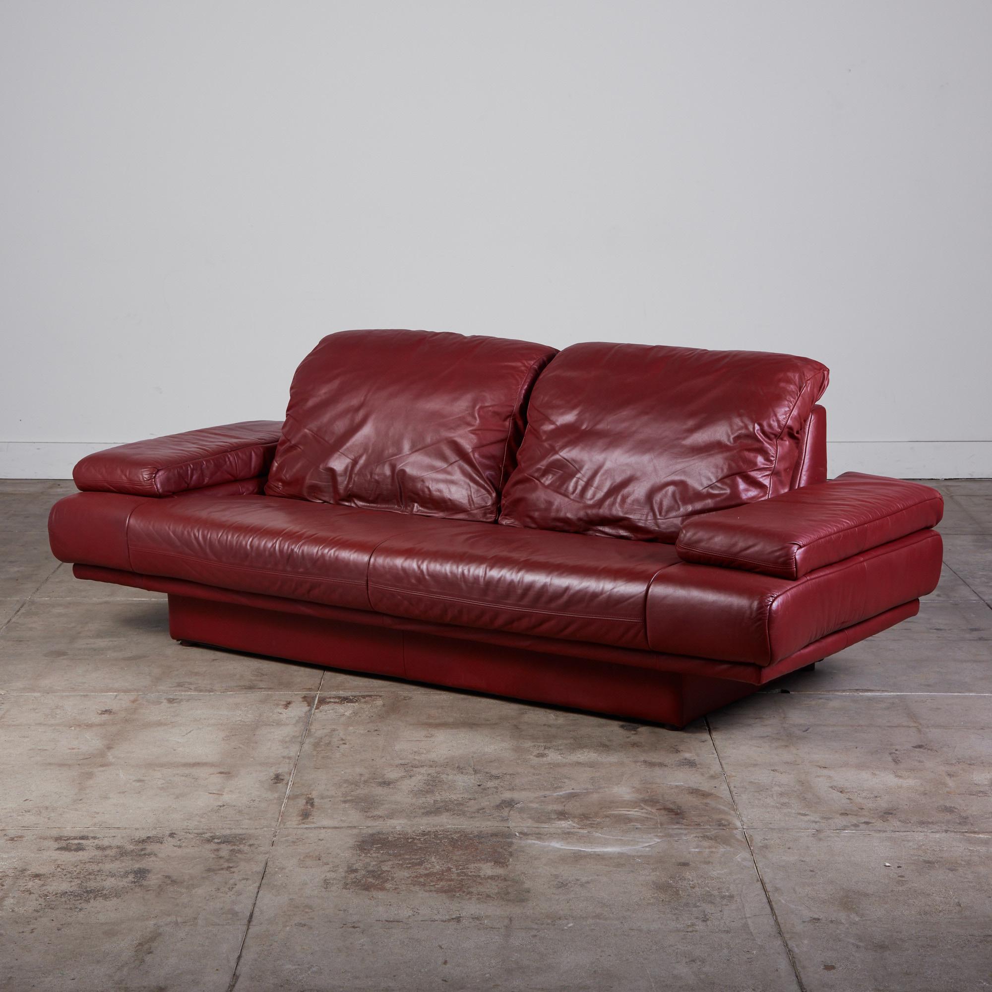 Postmodernes rotes Ledersofa im Stil von Rolf Benz. Das Sofa zeichnet sich durch ein minimalistisches, niedriges und breites Profil und Armlehnen aus, die mit einem weichen roten Leder bezogen sind. Die Kissen sitzen auf einem gepolsterten