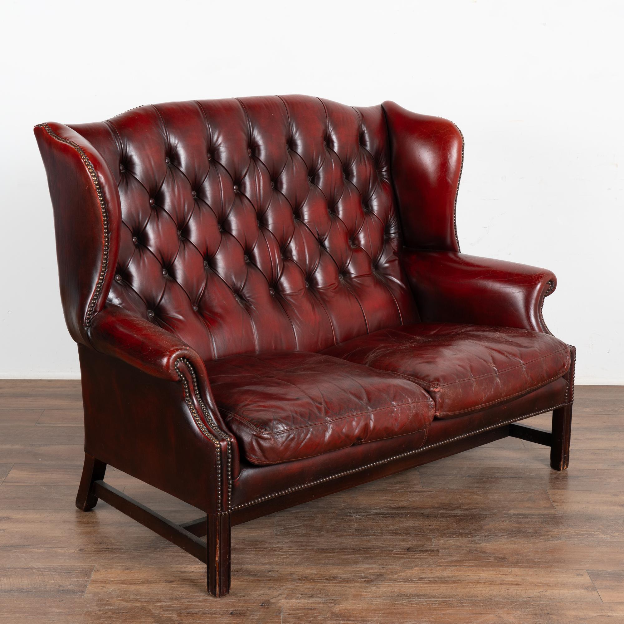 It is the deep red color of the vintage leather that captures your attention in this wonderful wingback Chesterfield loveseat or 