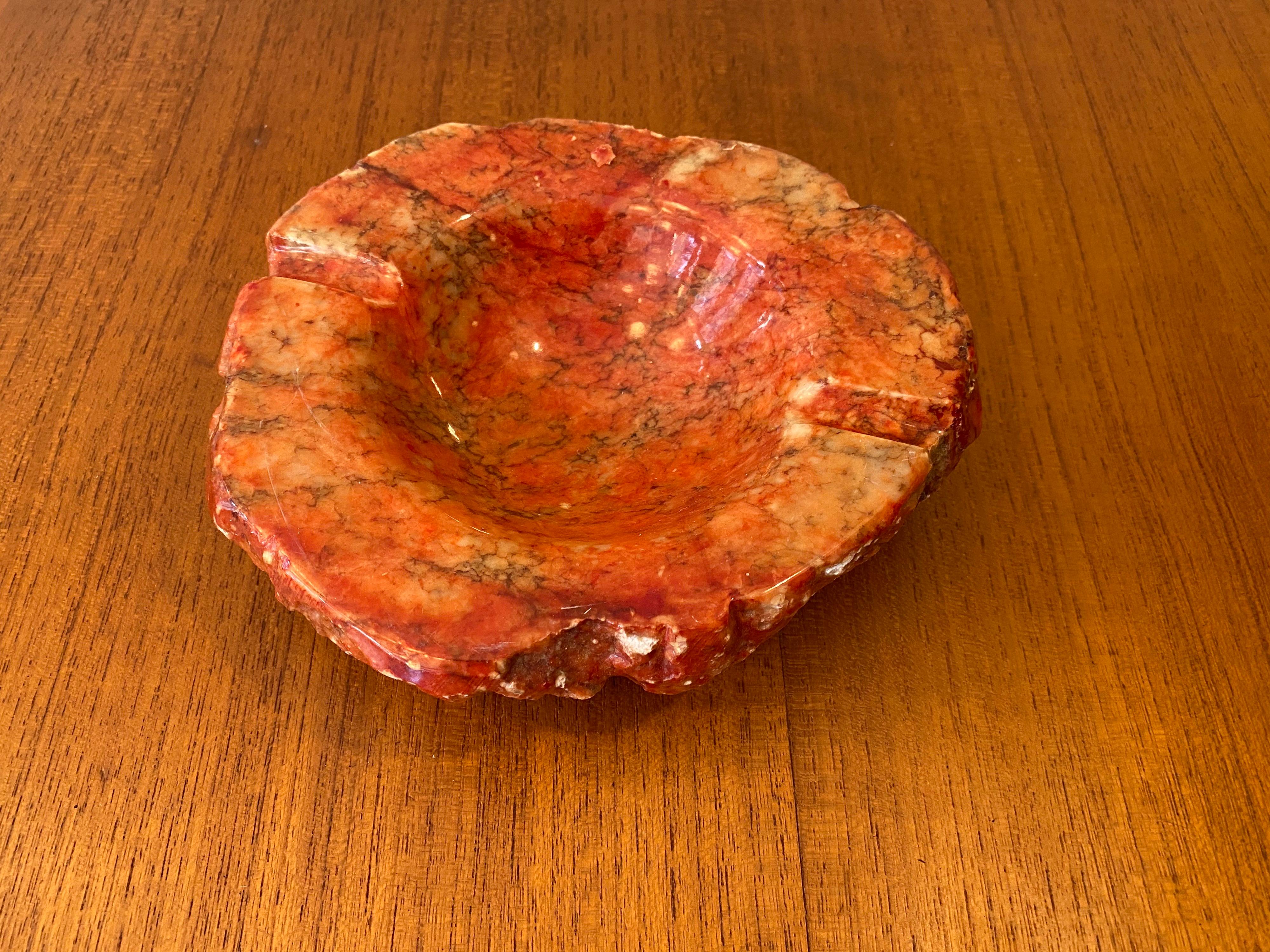 Red marble ashtray with rough carved sides.