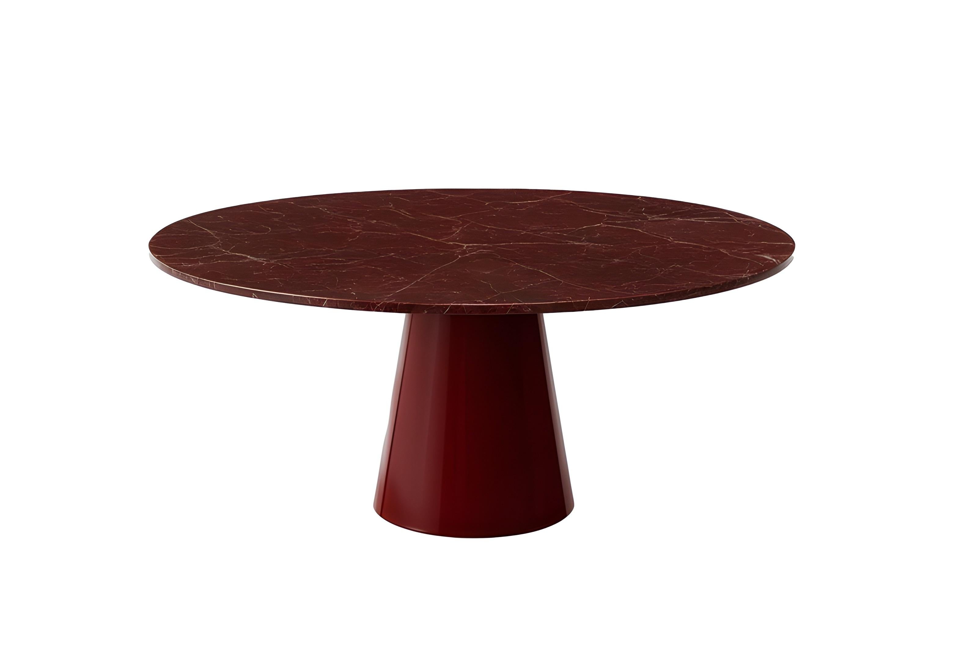 La elegante mesa de comedor redonda combina la presencia escultural con el lujo de los materiales refinados.
Su parte superior circular está hecha de mármol rojo ricamente veteado, que revela un movimiento natural en tonos carmesí, sangre de buey y