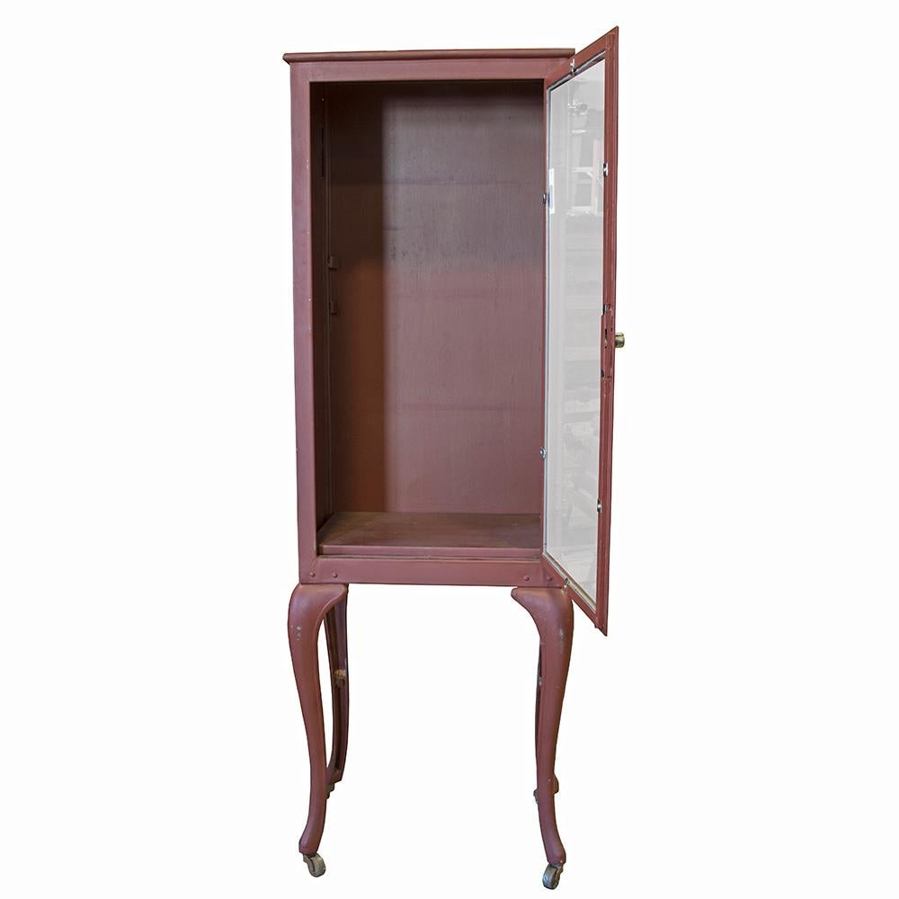 This early 20th century freestanding medicine cabinet has a graceful silhouette with gently curved legs. It has been repainted a shade of matte red and fitted with casters and a locking door.