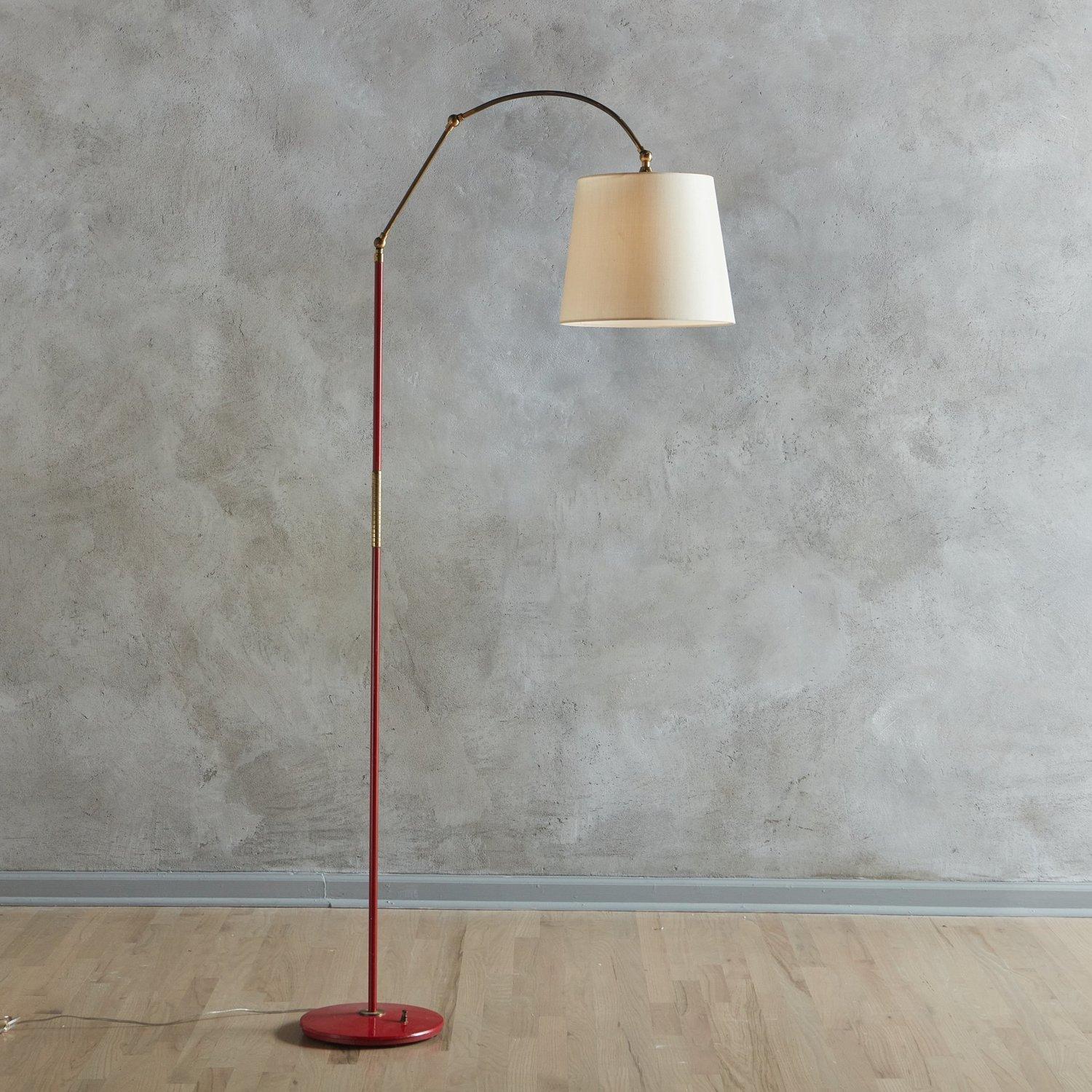 A 1960s Italian floor lamp in the style of Angelo Lelli featuring a sleek tubular red metal body with a circular base. This lamp has a patinated brass pivoting and adjustable arm with two joints, which allows the light to be directed in a variety of