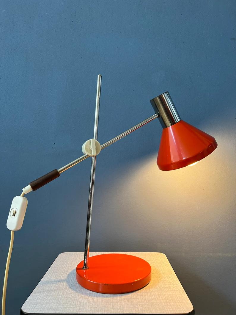 Red mid century desk lamp with adjustable swing arm. The arm can be fixated in any way desirable. The lamp is made out of metal and has a switch build into the cable. The lamp requires one E27/26 (standard) lightbulb and currently has an EU