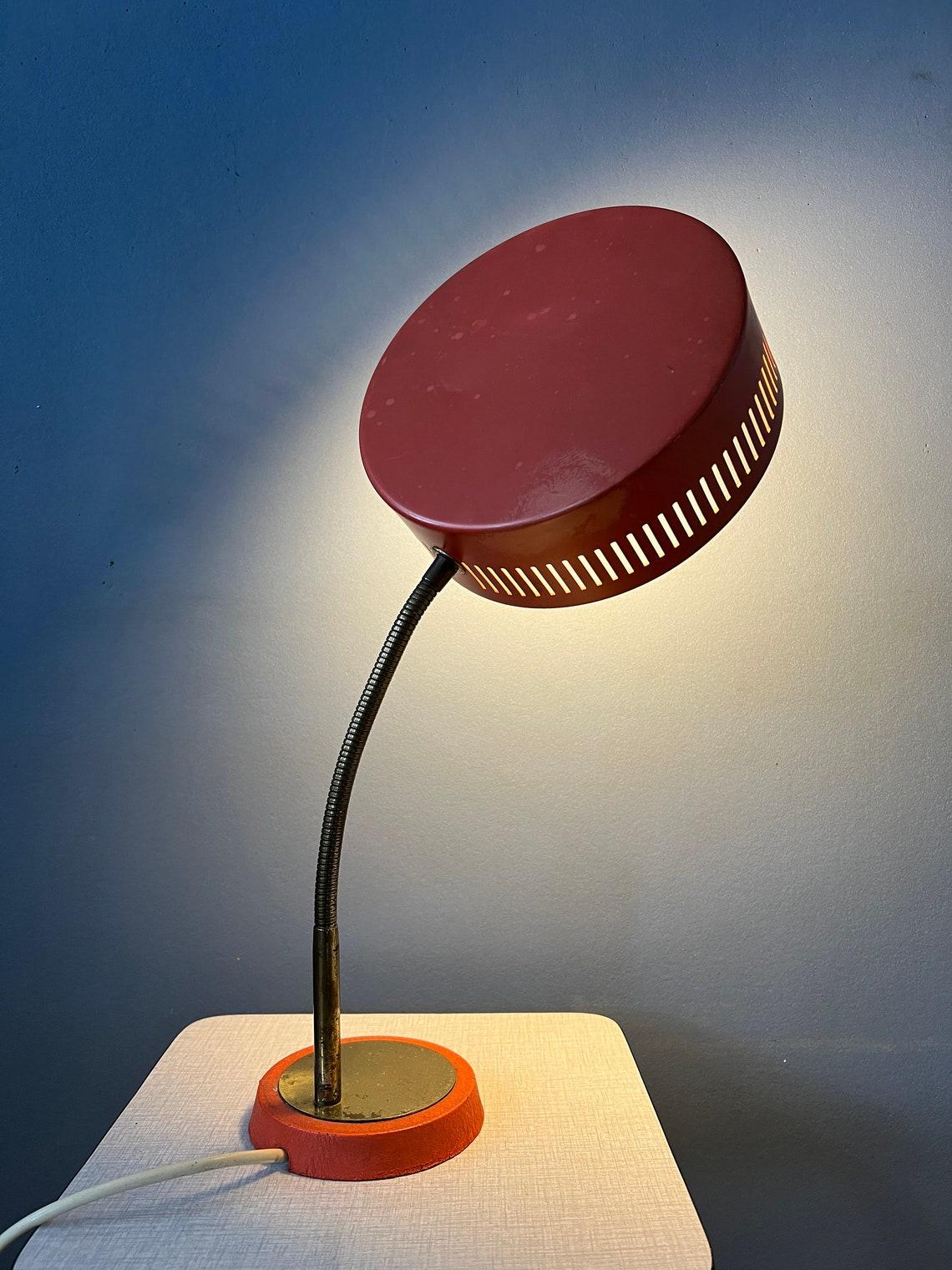 Red space age table lamp with flexible arm and adjustable shade. The arm and shade can be positioned in any way desirable, see pictures. Also the shade itself be repositioned. The light spreads very nicely through the roster on the side. The lamp