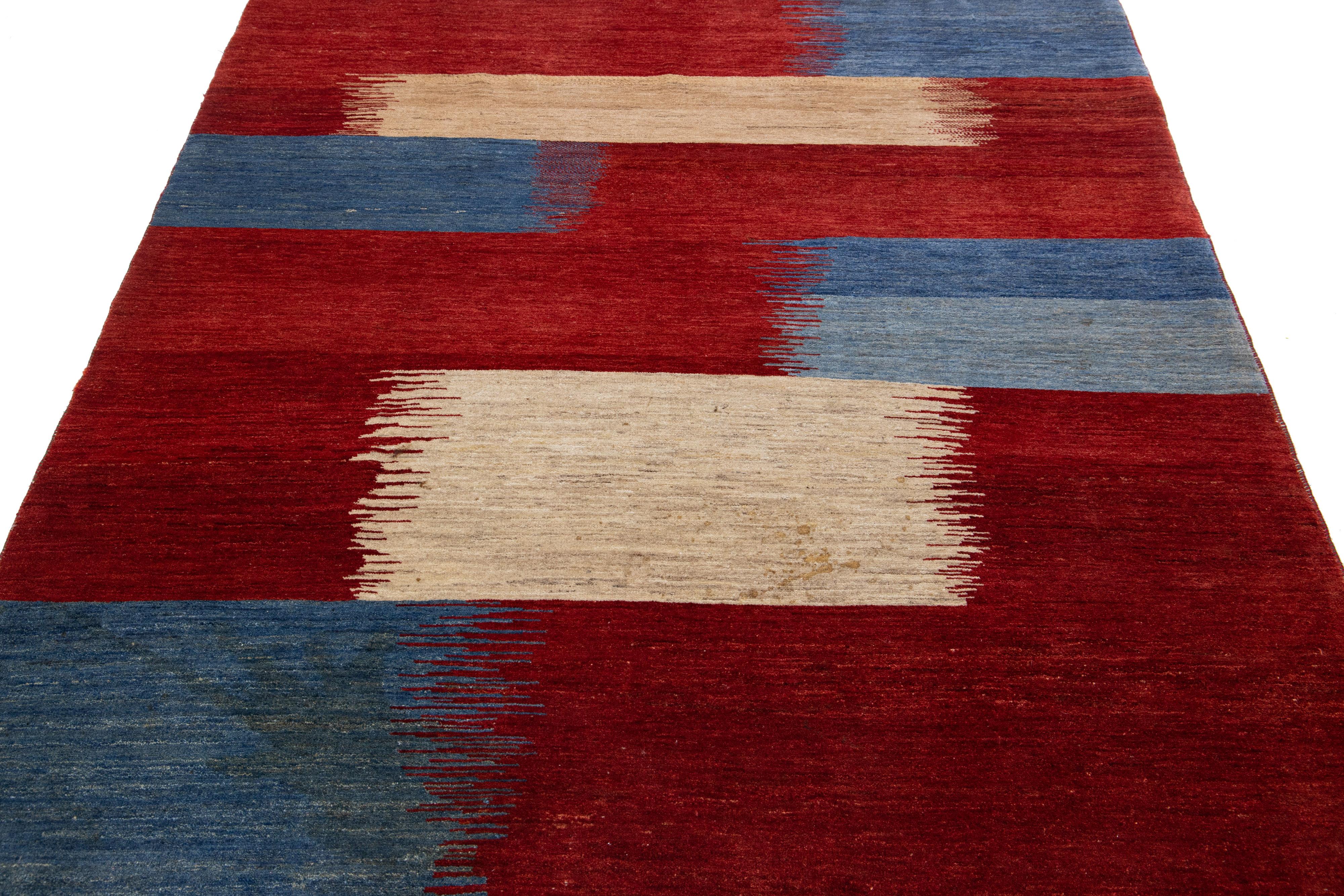 Beautiful modern Gabbeh-style hand-woven wool rug with a red color field. This piece has blue and beige accents in a gorgeous abstract design.

This rug measures: 5'2