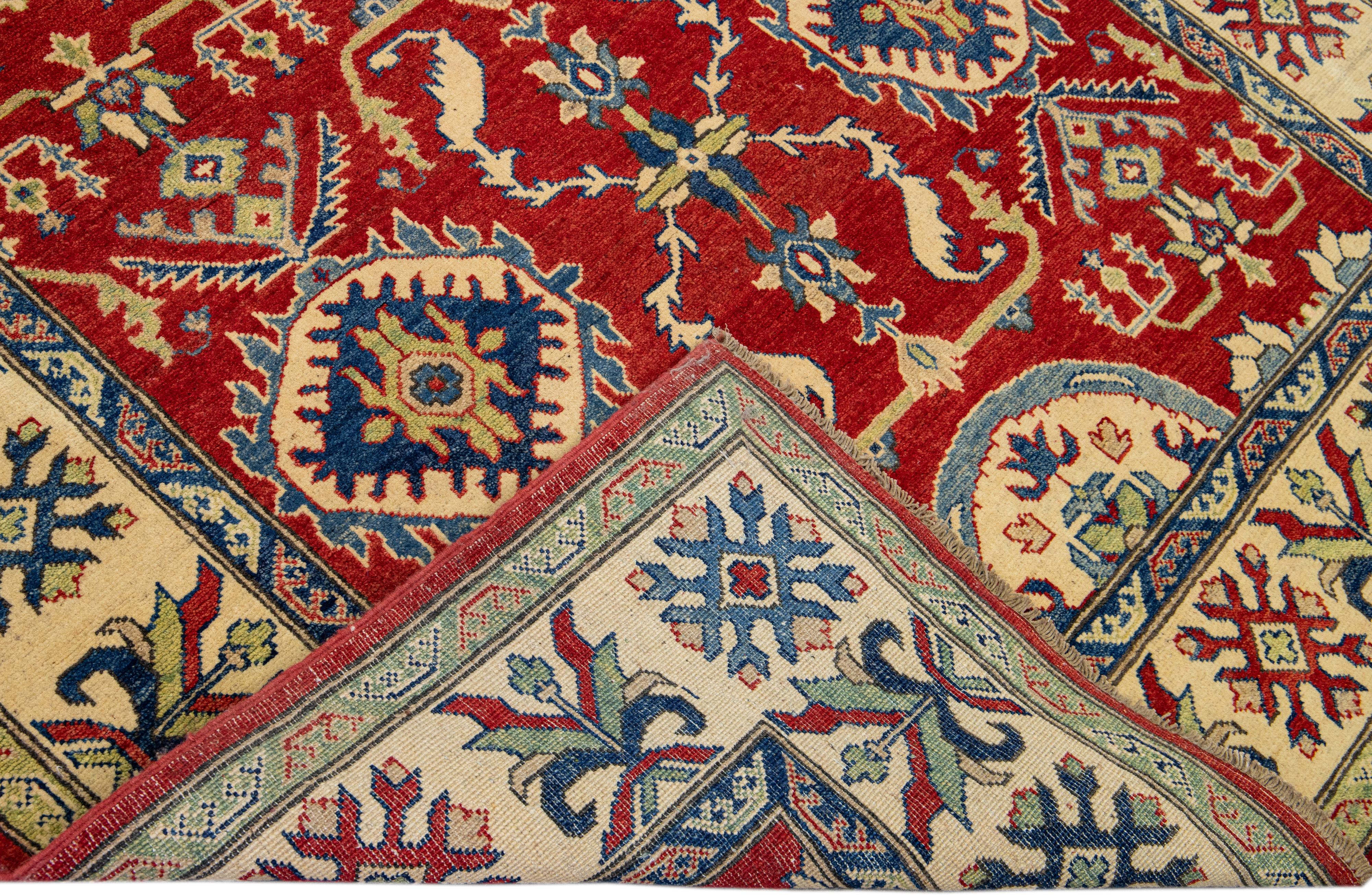 Beautiful modern Kazak hand-knotted wool rug with a red field. This rug has beige, blue, and green frame and accents that feature an all-over geometric design.

This rug measures: 5'6