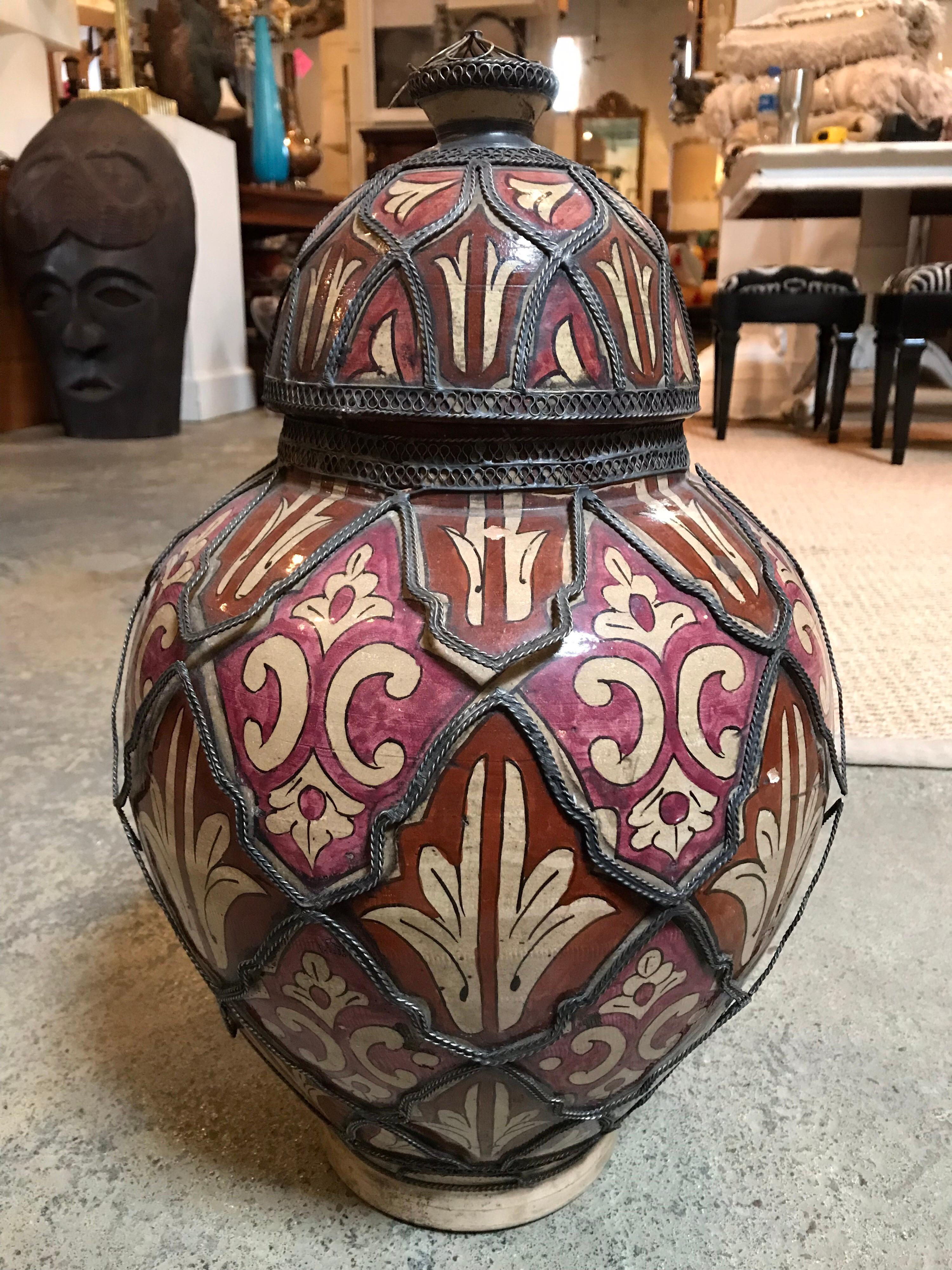 This vintage red Moroccan pot has white details painted on it and it is wrapped in decorative metal strips.