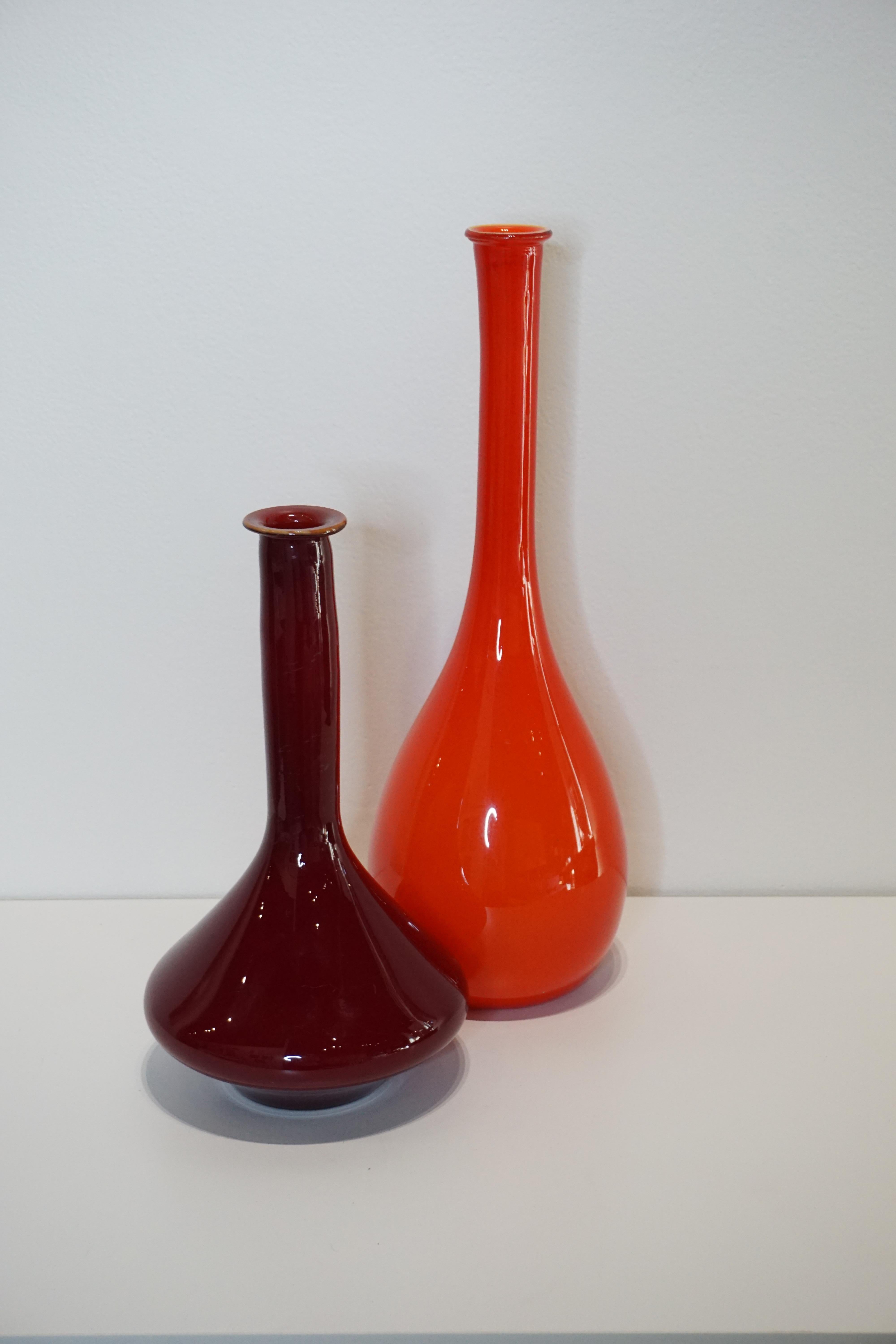 Red Murano glass vase with broad base featuring glass from the Venetian island of Murano, a place known for its production of vibrant and unique glass products.